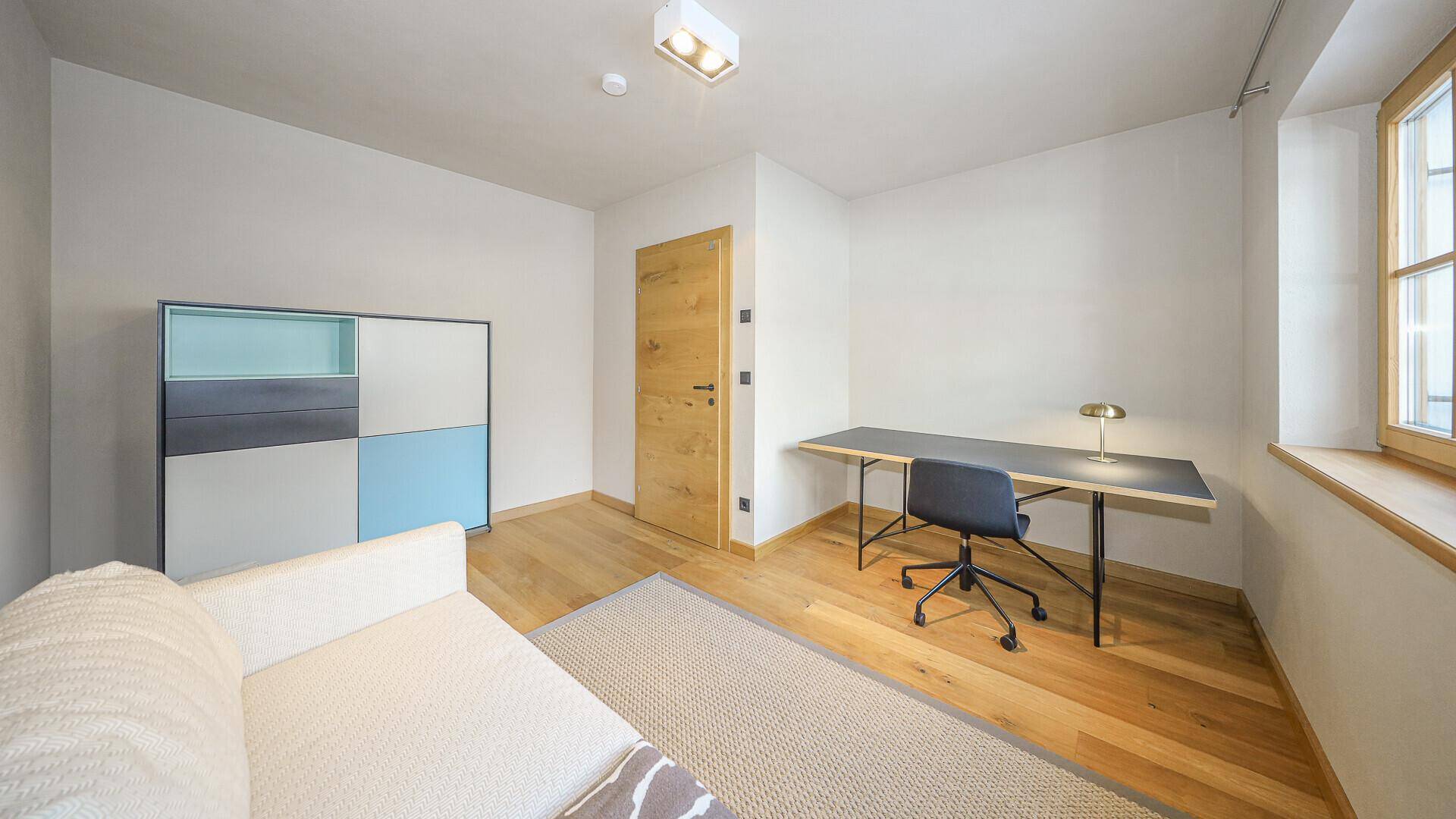 Helles Arbeitszimmer mit Holzboden, Schreibtisch und Fenster mit Blick nach draußen.