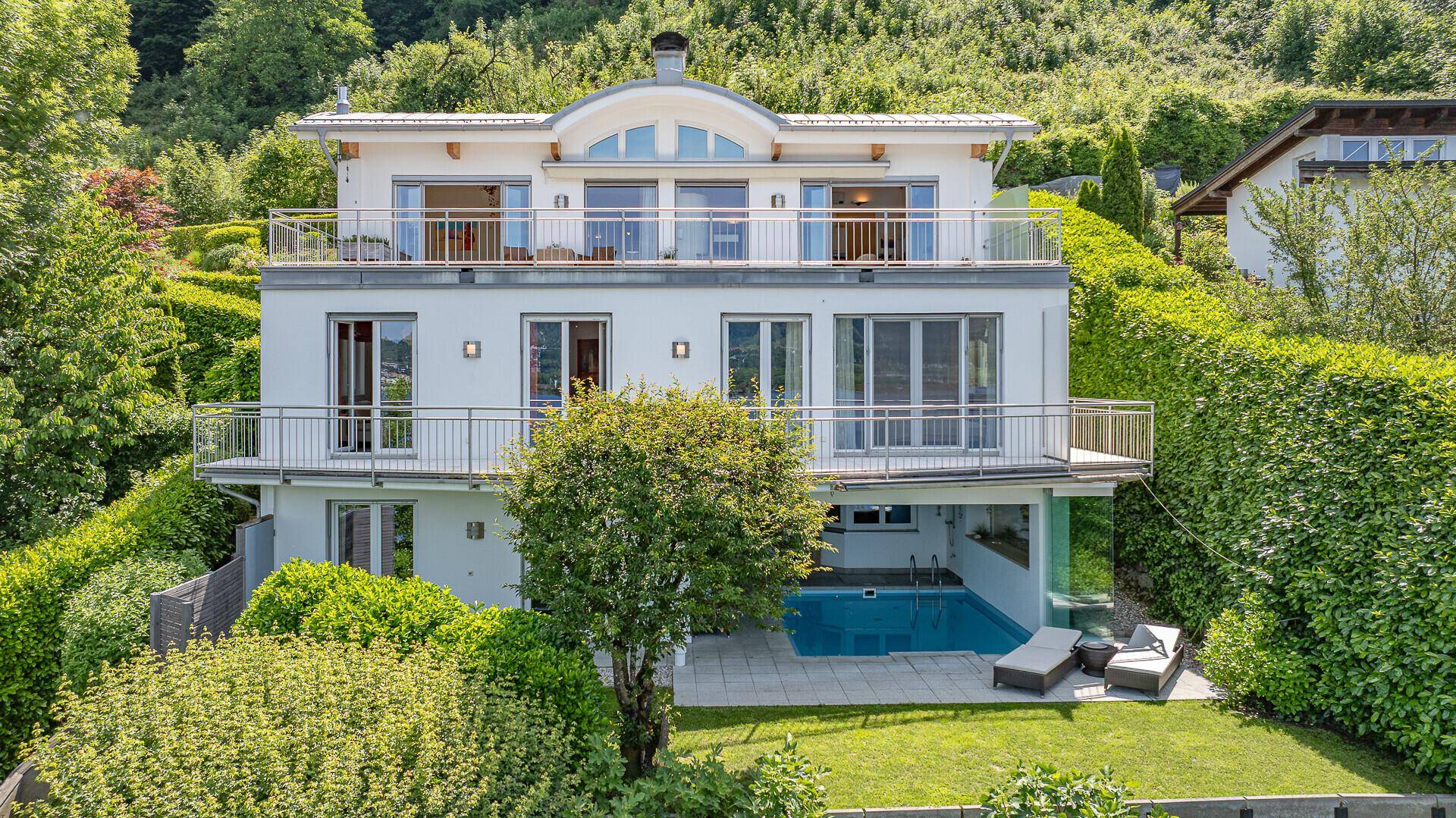 Moderne Villa mit mehreren Balkonen und einem Poolbereich im Garten, umgeben von viel Grün.