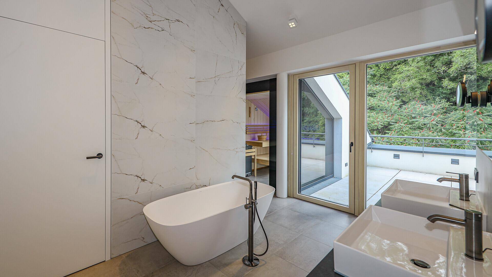 Modernes Badezimmer mit freistehender Badewanne, Doppelwaschbecken und Blick ins Grüne.