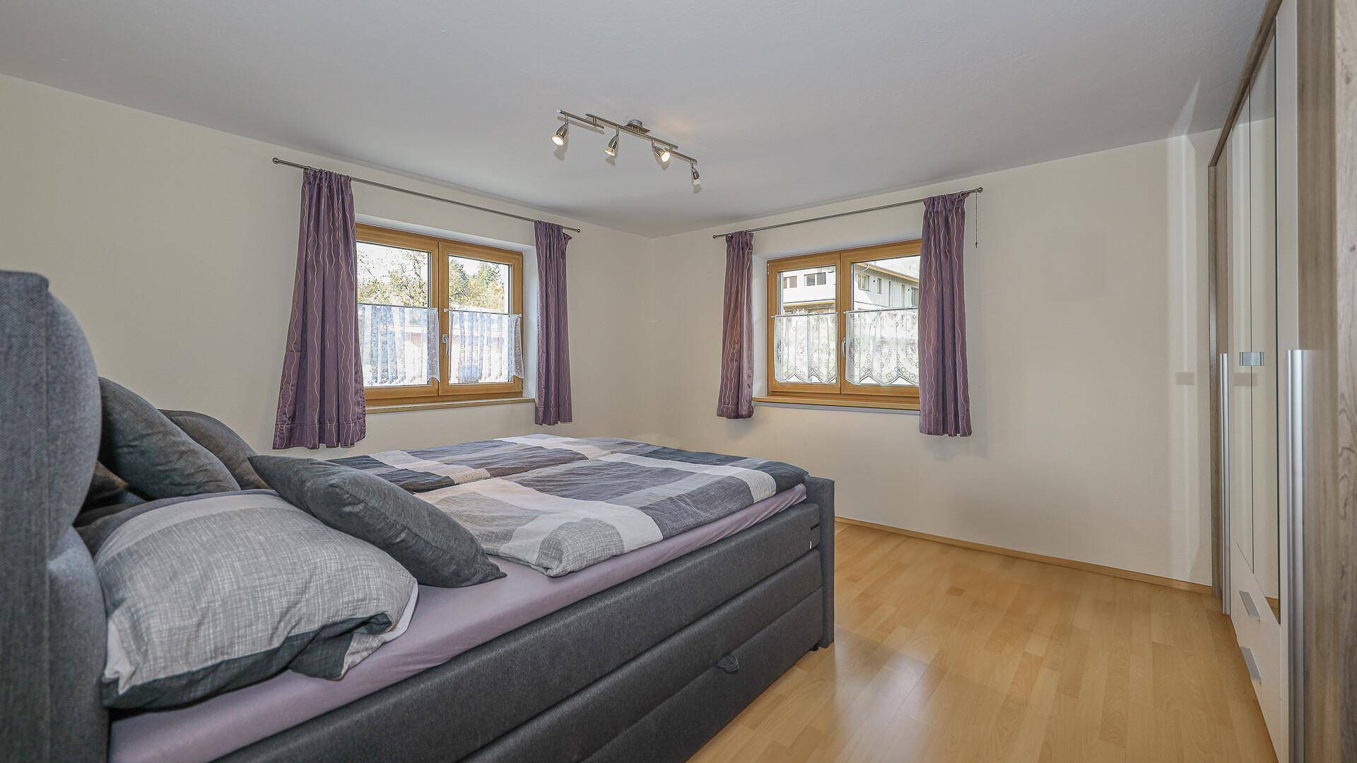 Helles Schlafzimmer mit Doppelbett, Holzfußboden und großen Fenstern.