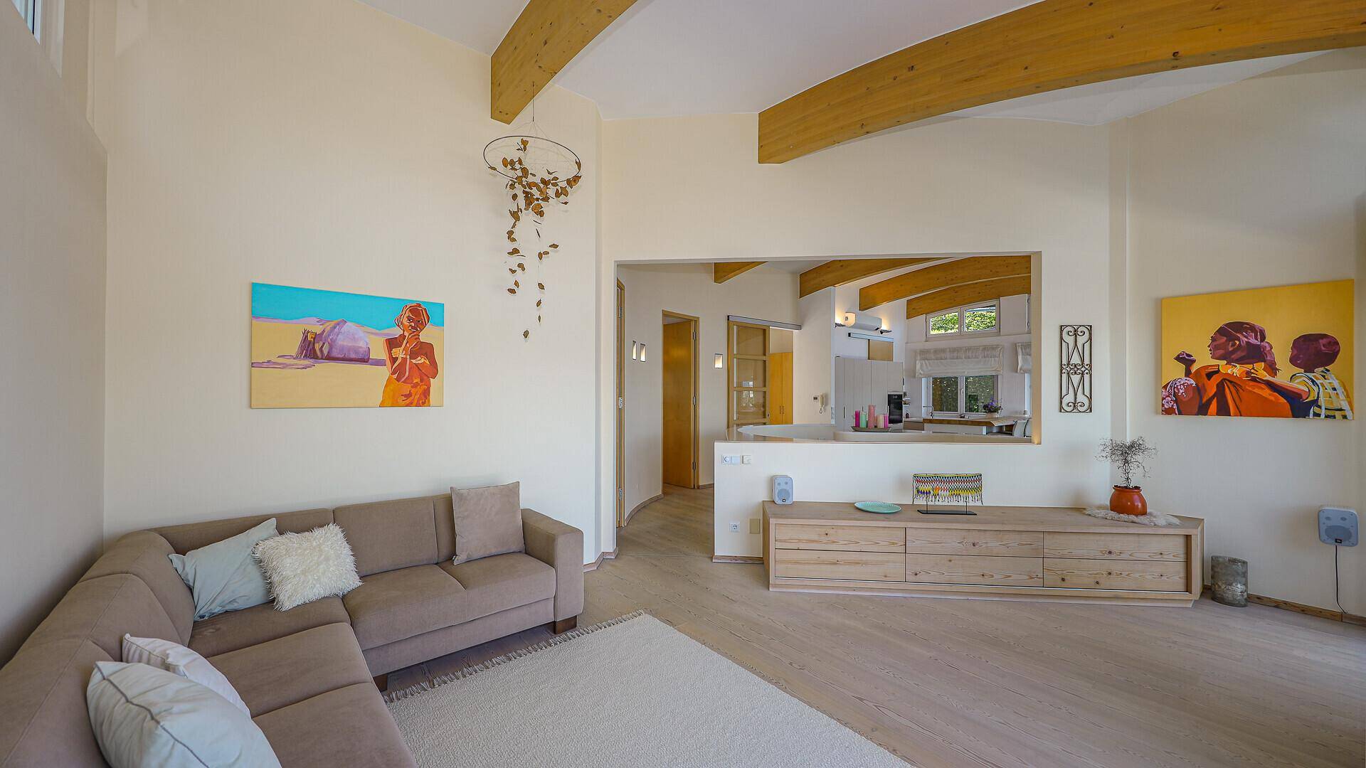 Gemütliches Wohnzimmer mit beigem Sofa, Holzbalken und Blick auf den offenen Küchenbereich.