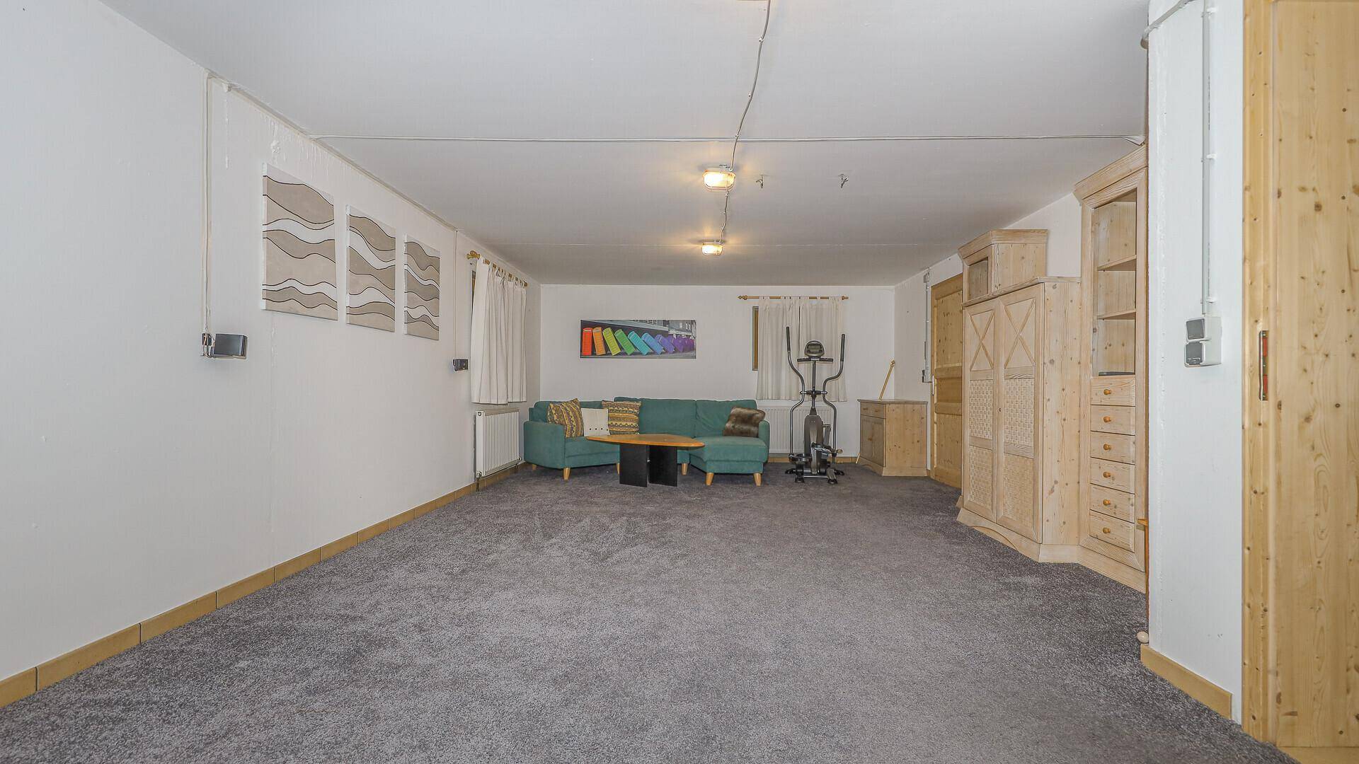 Geräumiger Kellerraum mit Teppichboden, Sofa und Fitnessgerät, ideal als Hobbyraum.
