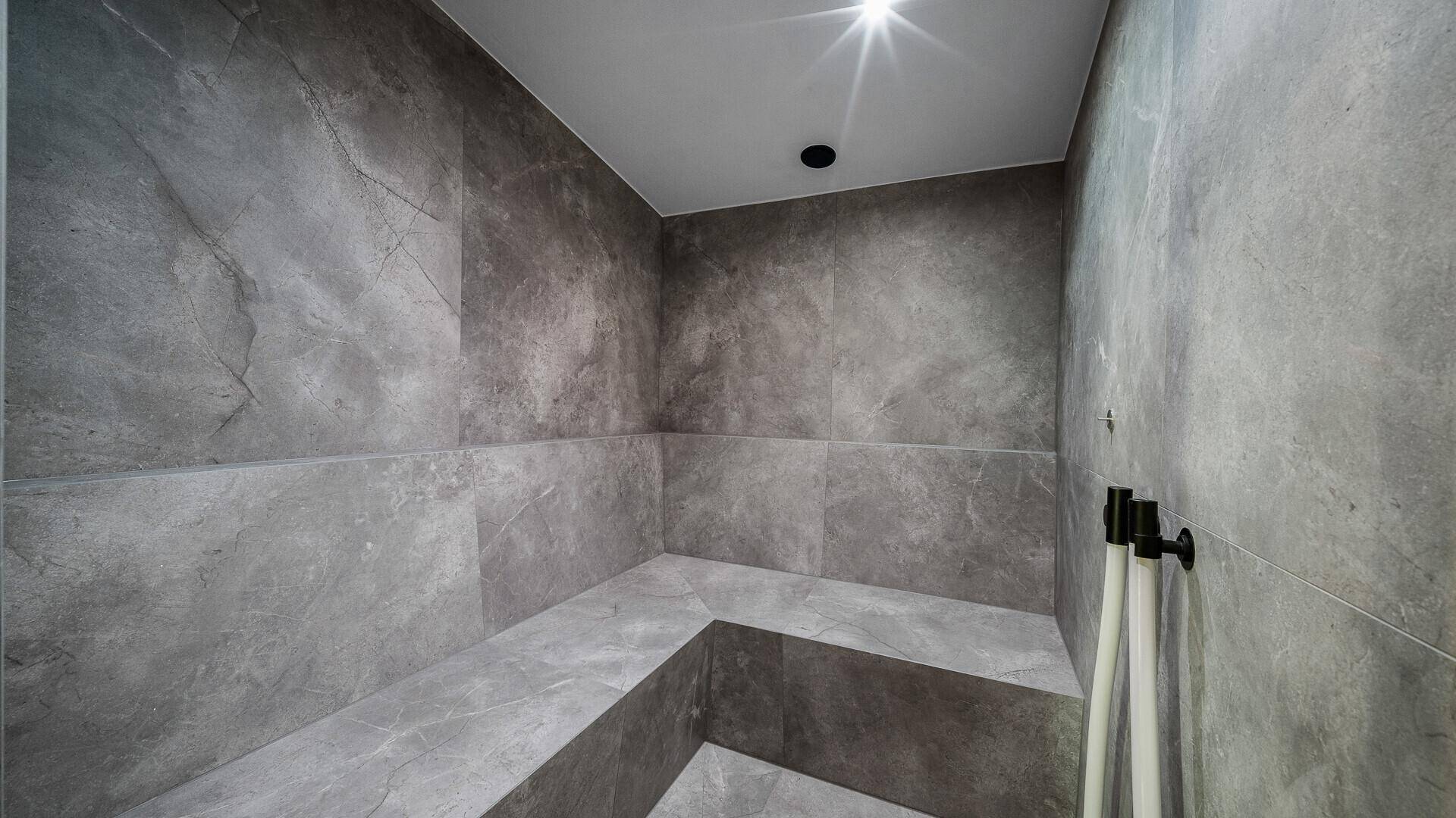 Modernes Dampfbad mit grauen Fliesen und Sitzgelegenheiten für Wellness.