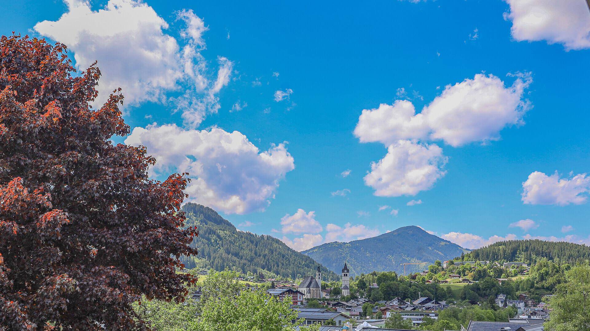 Panoramablick auf eine malerische Berglandschaft mit einem Dorf im Tal unter blauem Himmel.