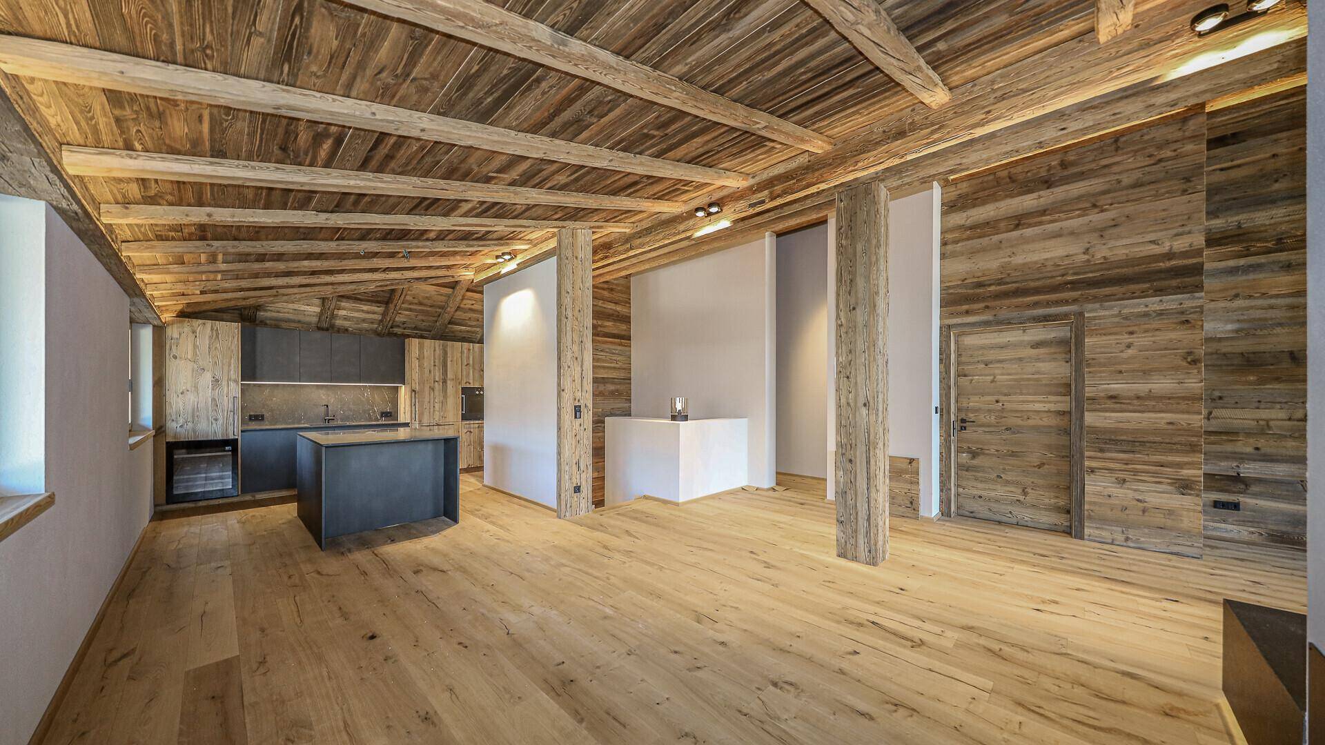 Großer offener Wohnbereich mit Holzbalkendecke und integrierter moderner Küche.
