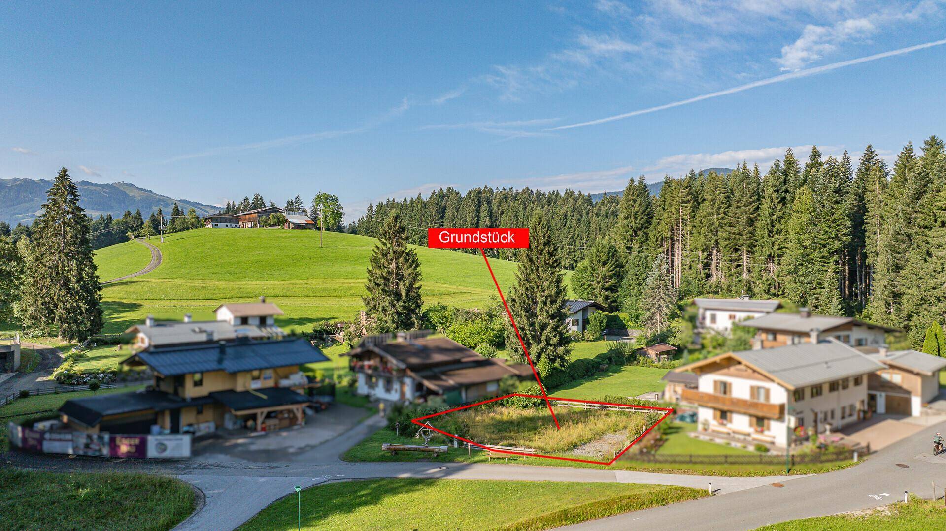 Nahaufnahme des Baugrundstücks in ländlicher Umgebung mit angrenzenden Häusern und Straße.