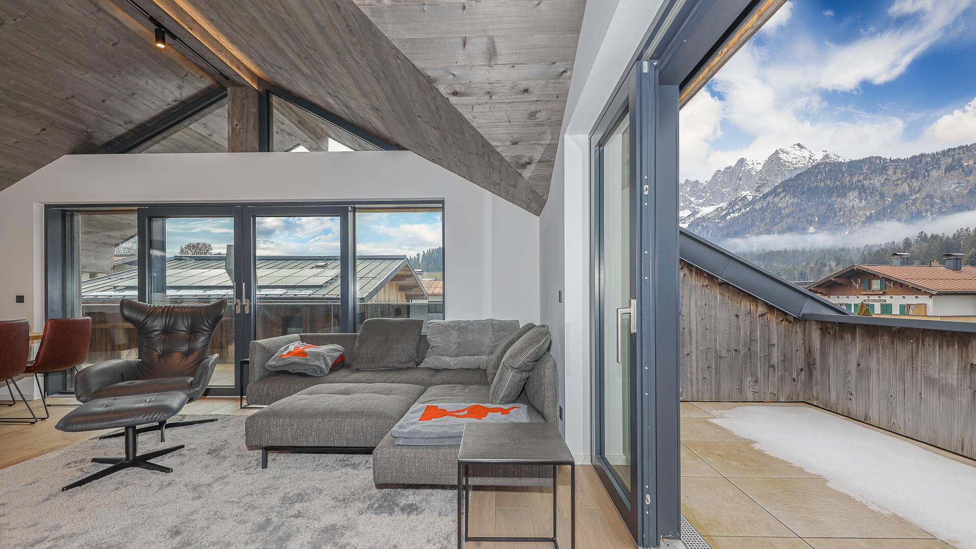 Heller Wohnbereich mit großem Sofa und direktem Zugang zu einem Balkon mit Bergblick.