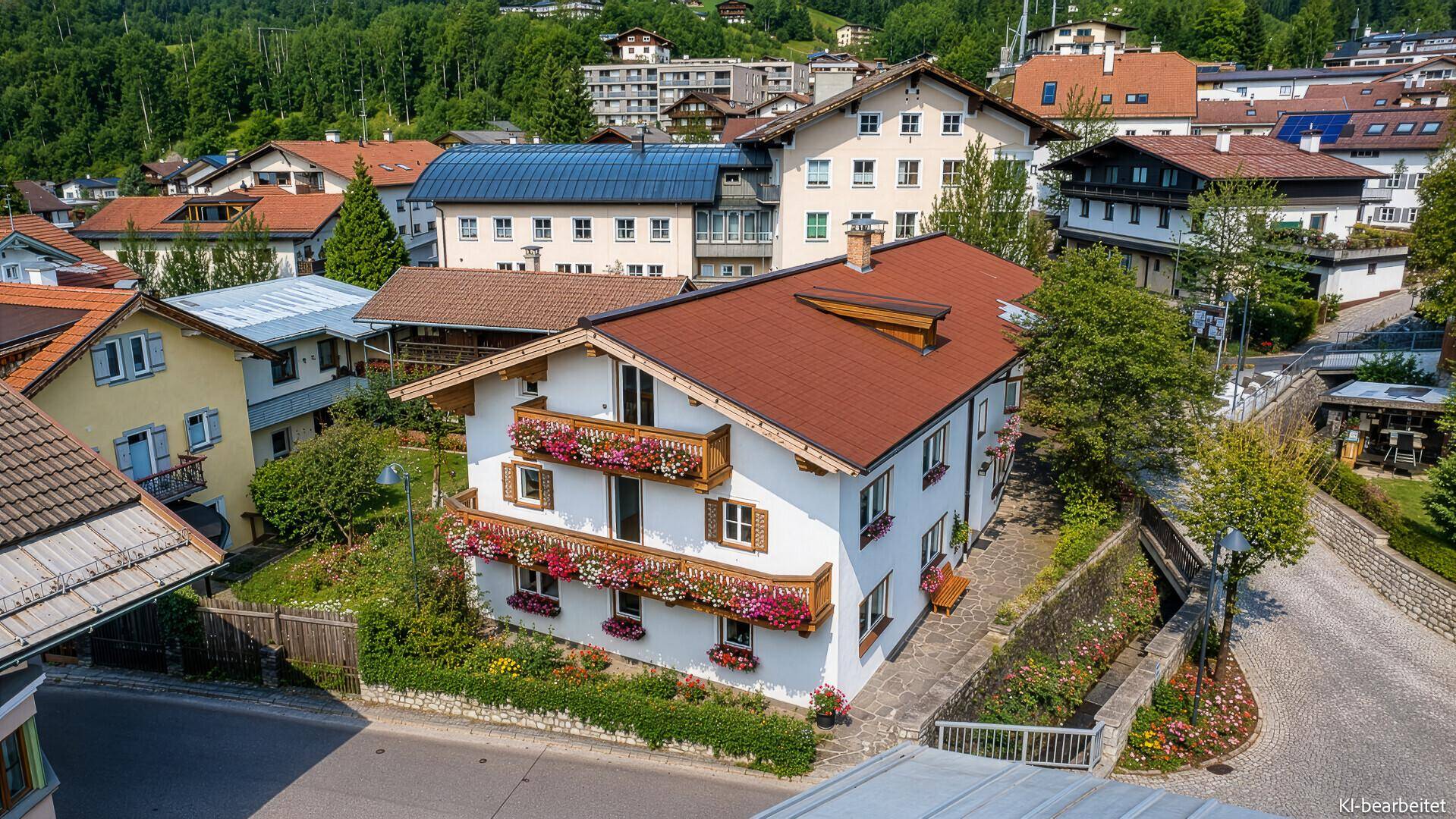 Vogelperspektive eines charmanten Hauses mit blühenden Balkonen und rotem Dach in einer Berglandschaft.