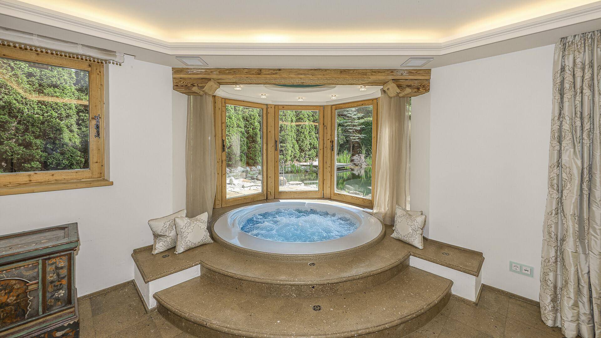 Luxuriöser Whirlpool in einem hellen Raum mit Blick auf den Garten.