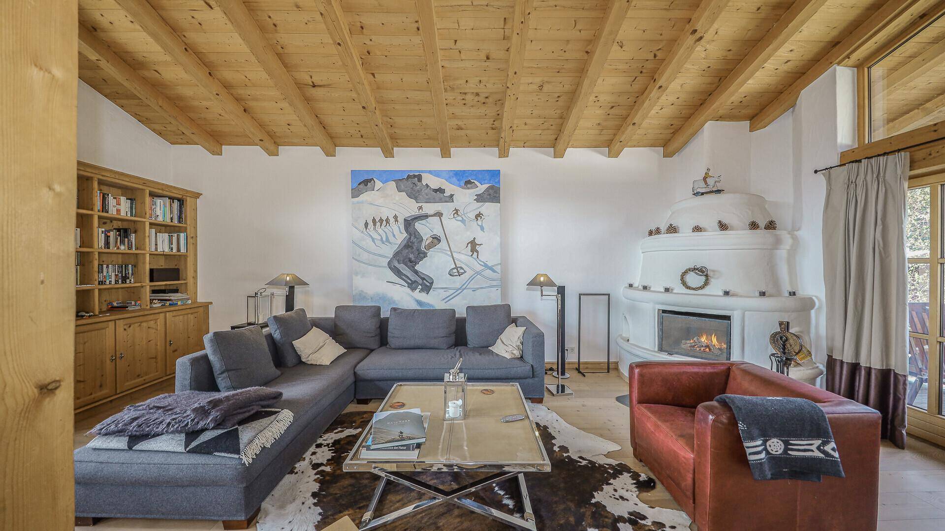 Helles Wohnzimmer mit Kachelofen, Holzbalkendecke und großem Sofa im alpinen Stil.