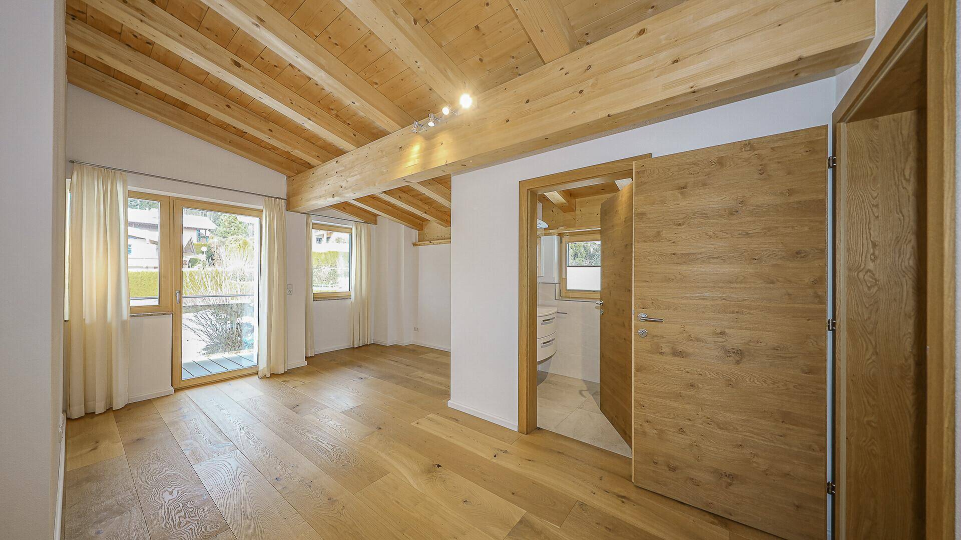 Helles Schlafzimmer im Dachgeschoss mit Holzbalkendecke, Holzboden und Zugang zu einem Badezimmer.