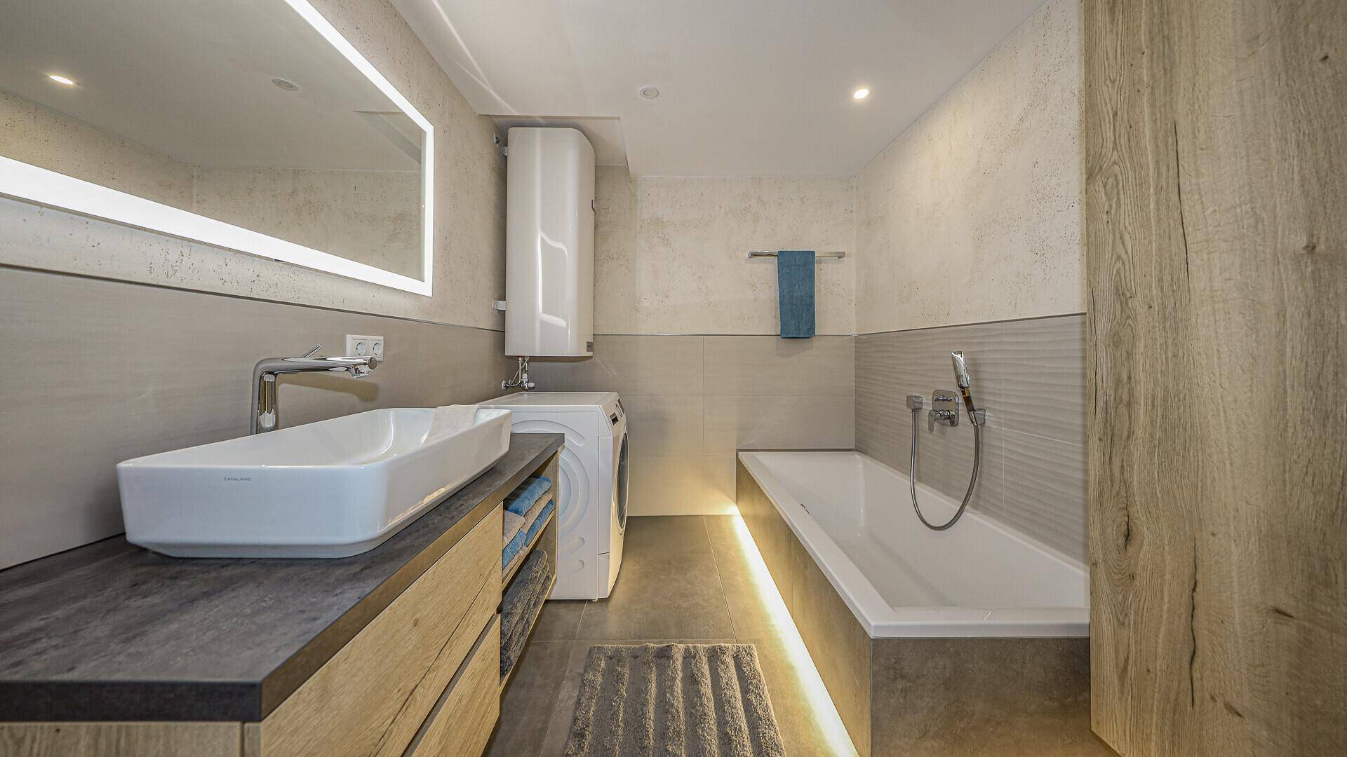 Modernes Badezimmer mit großem Waschbecken, Badewanne und integrierter Beleuchtung.