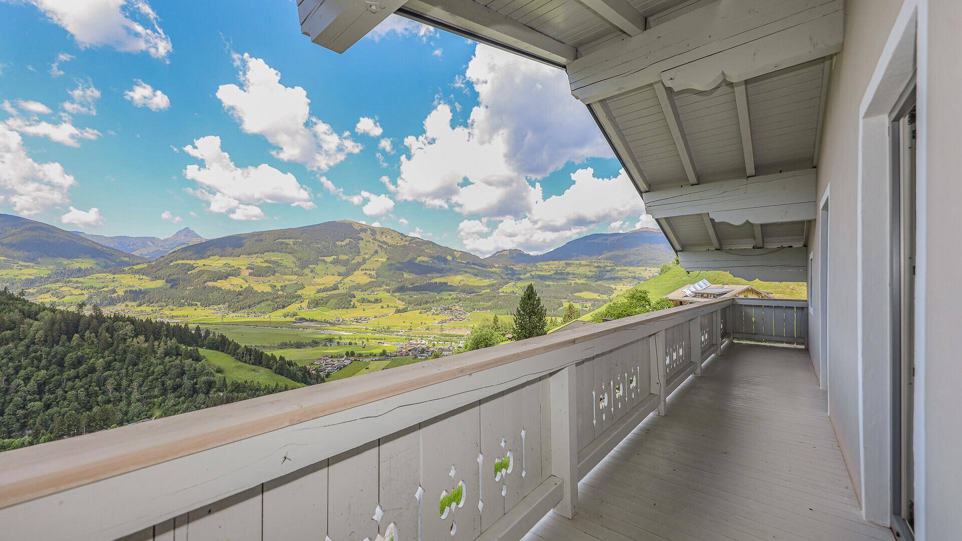 Langer Balkon mit traditionellem Holzgeländer und weitem Blick über das Tal und die Berge.