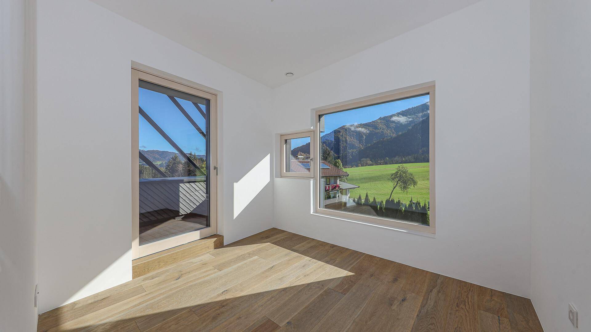 Helles Zimmer mit Holzboden und Zugang zu einem Balkon mit Bergblick.