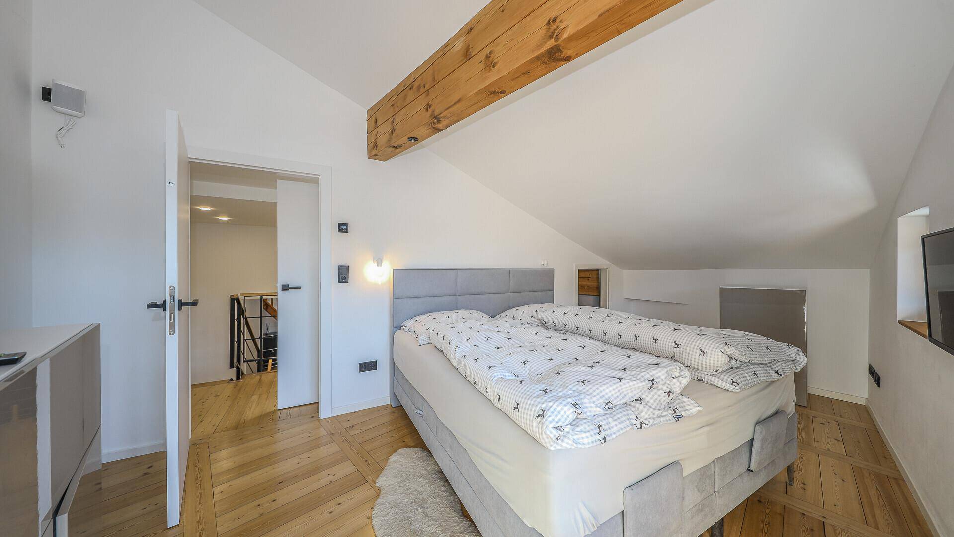 Gemütliches Schlafzimmer im Dachgeschoss mit schräger Decke, Holzbalken und komfortablem Doppelbett.