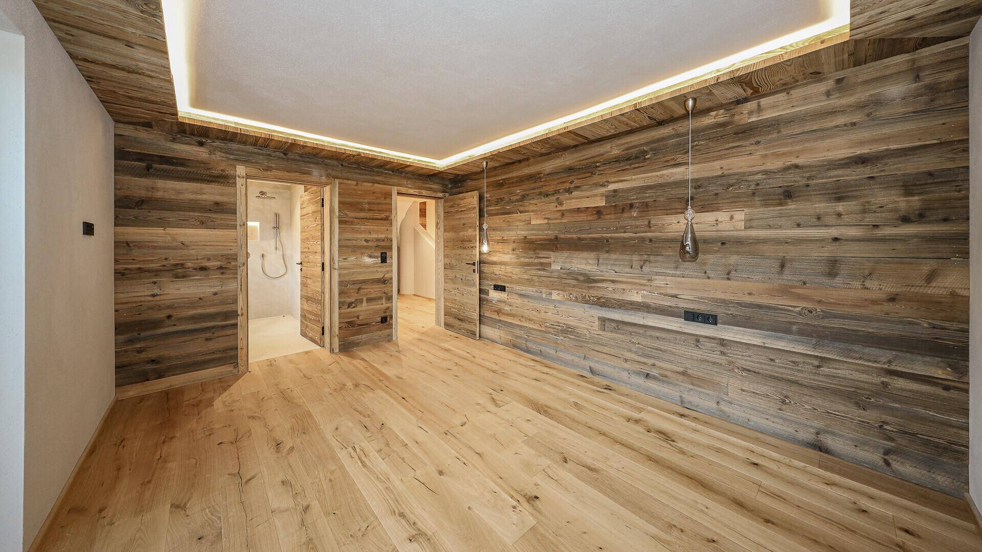 Geräumiges Schlafzimmer mit Holzwänden und Holzboden, bietet Zugang zu zwei weiteren Räumen.