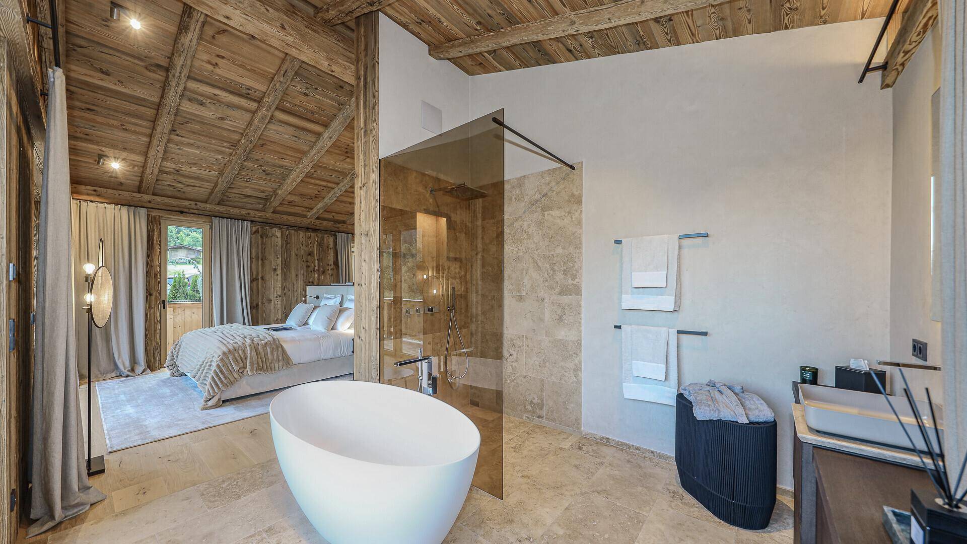 Offenes Badezimmer mit freistehender Badewanne, begehbarer Dusche und Blick ins Schlafzimmer.