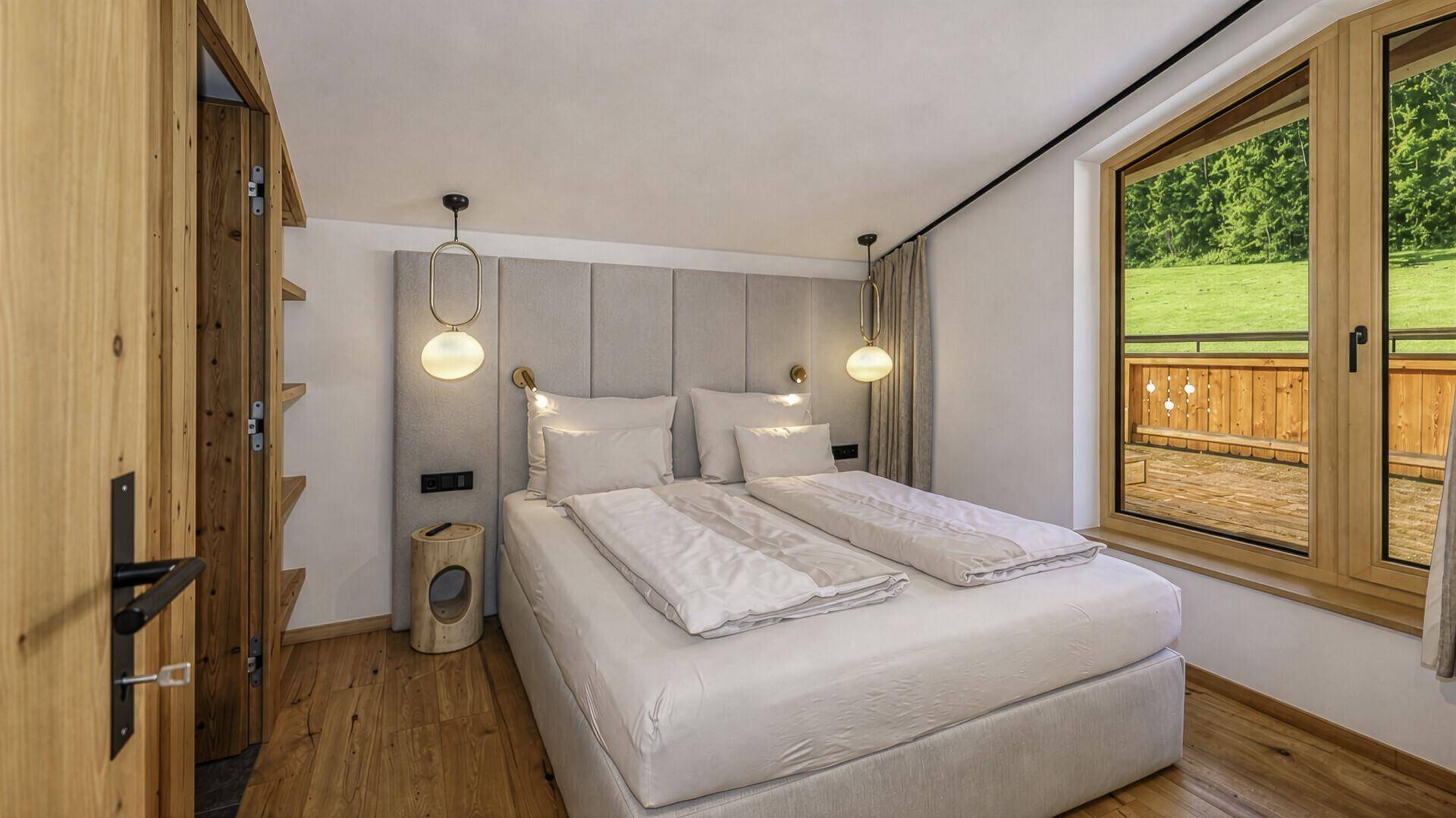 Helles Schlafzimmer mit Doppelbett, Holzboden und Blick auf die Terrasse und grüne Umgebung.