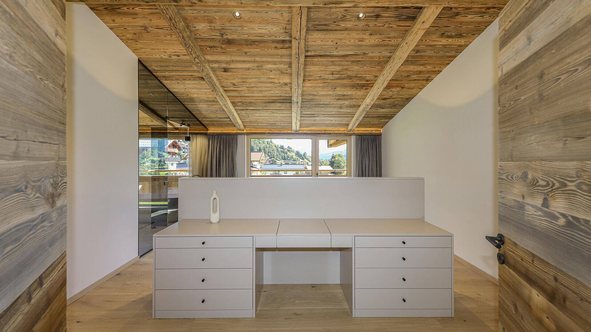 Heller Ankleidebereich oder Arbeitsplatz mit Einbauschränken und Holzbalkendecke.