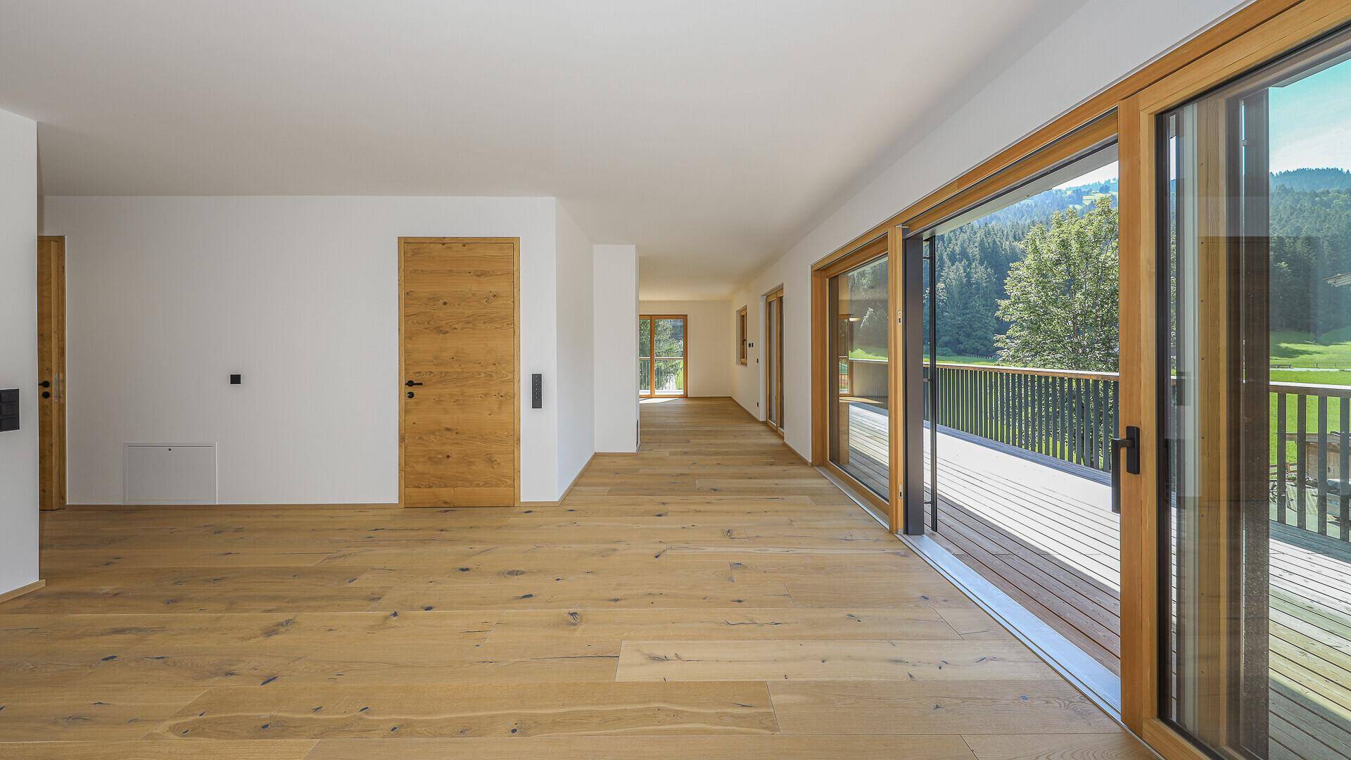 Langer Flur mit Holzboden und großen Schiebetüren, die zu einer Terrasse führen.