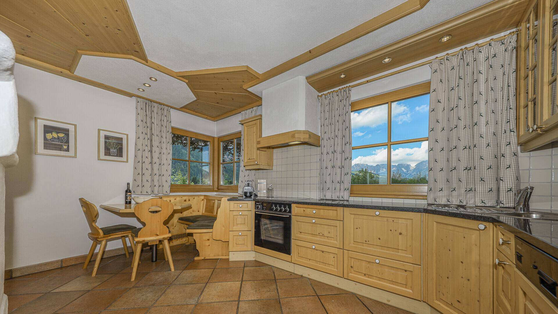 Traditionelle Küche mit Holzeinbauten, Essbereich und malerischem Bergblick aus dem Fenster.