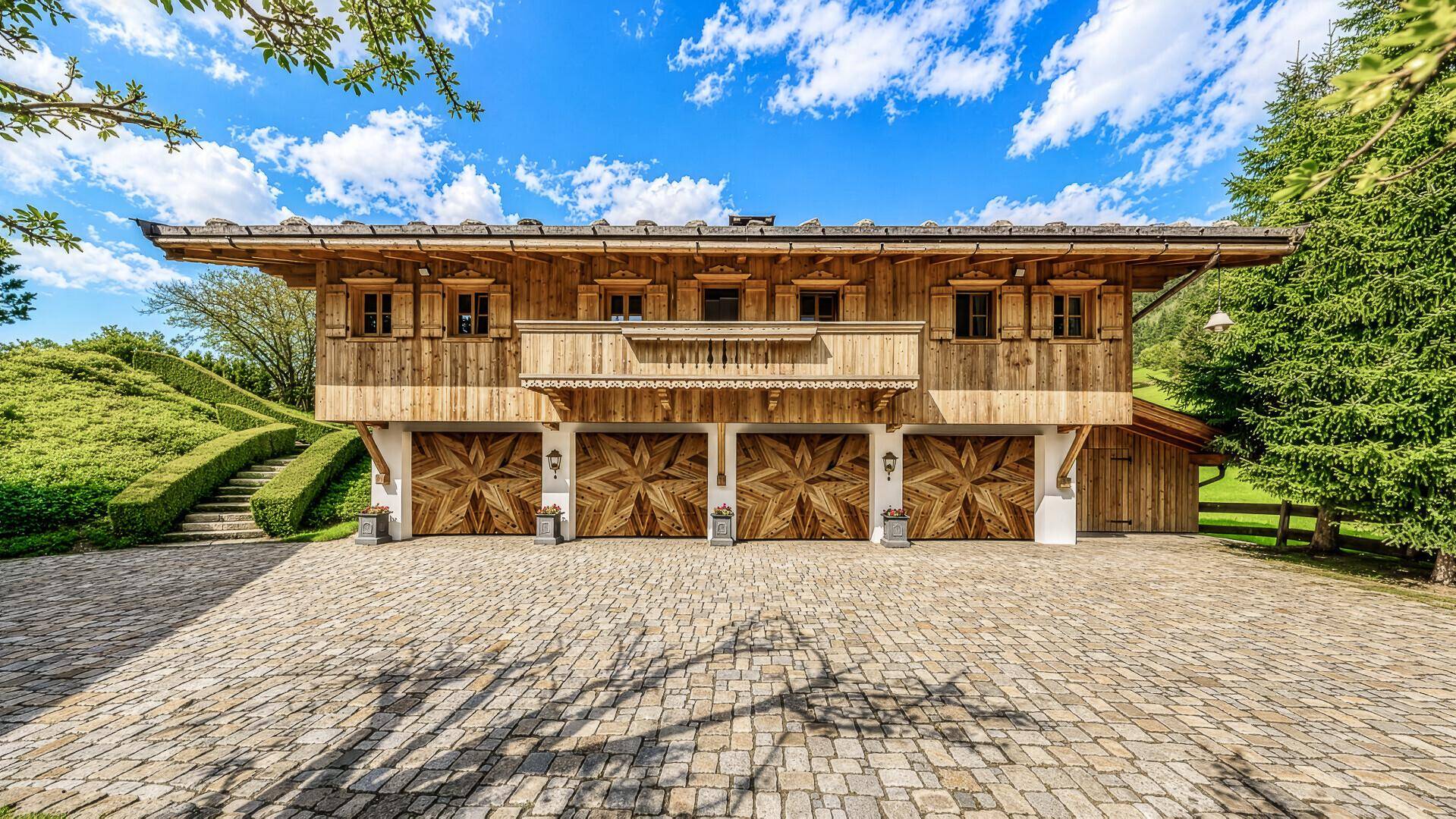Großzügige Garage mit vier Holztoren und gepflasterter Zufahrt, passend zum alpinen Stil.