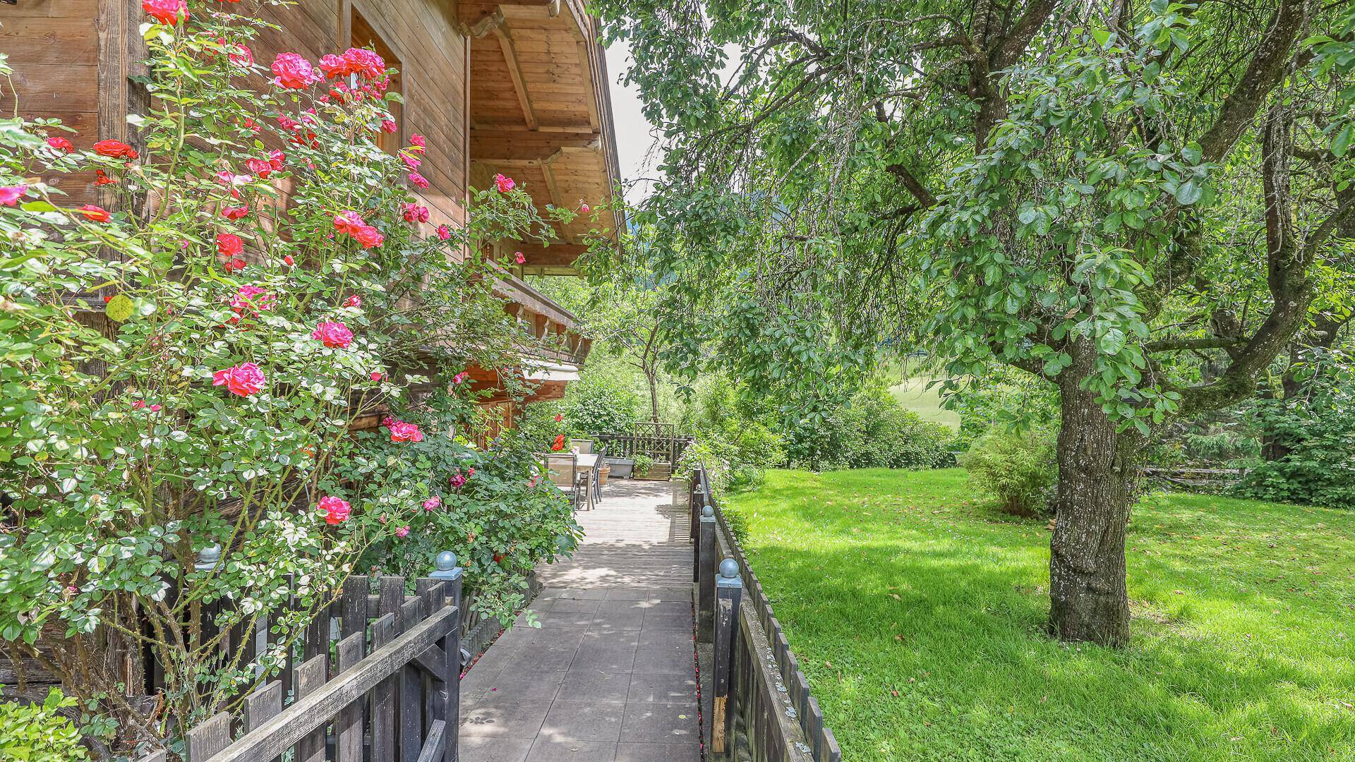 Malerischer Gartenweg entlang des Hauses mit blühenden Rosen und altem Baumbestand.