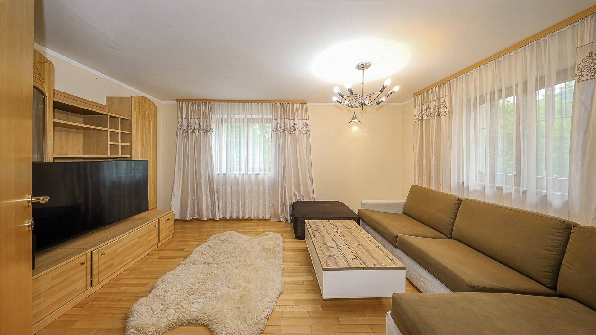 Gemütliches Wohnzimmer mit hellem Holzfußboden, beiger Couch und moderner Deckenleuchte.