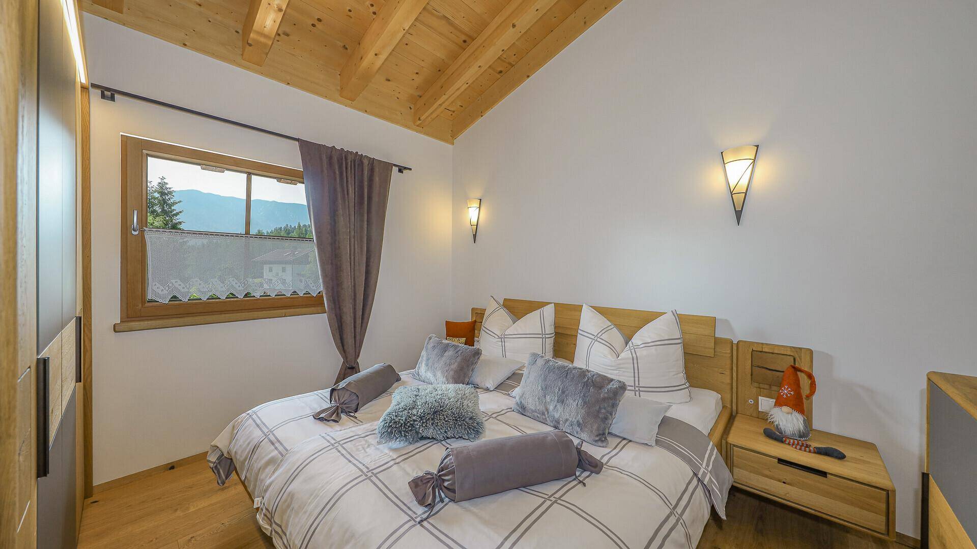 Gemütliches Schlafzimmer mit Doppelbett, Holzmöbeln und einem Fenster mit Blick auf die Berge.
