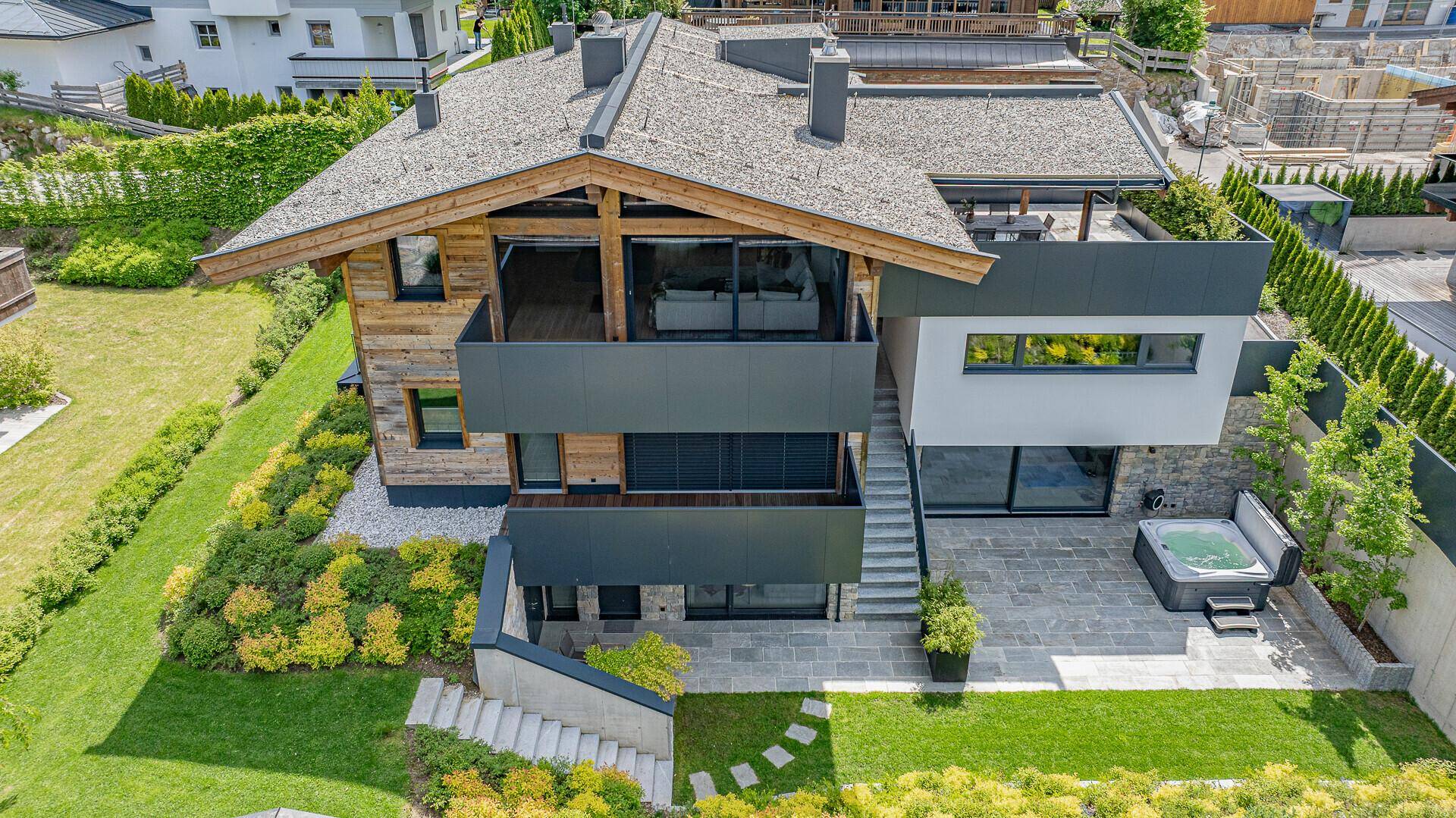 Vogelperspektive des modernen Chalets mit Garten, Terrasse und Whirlpool in alpiner Umgebung.