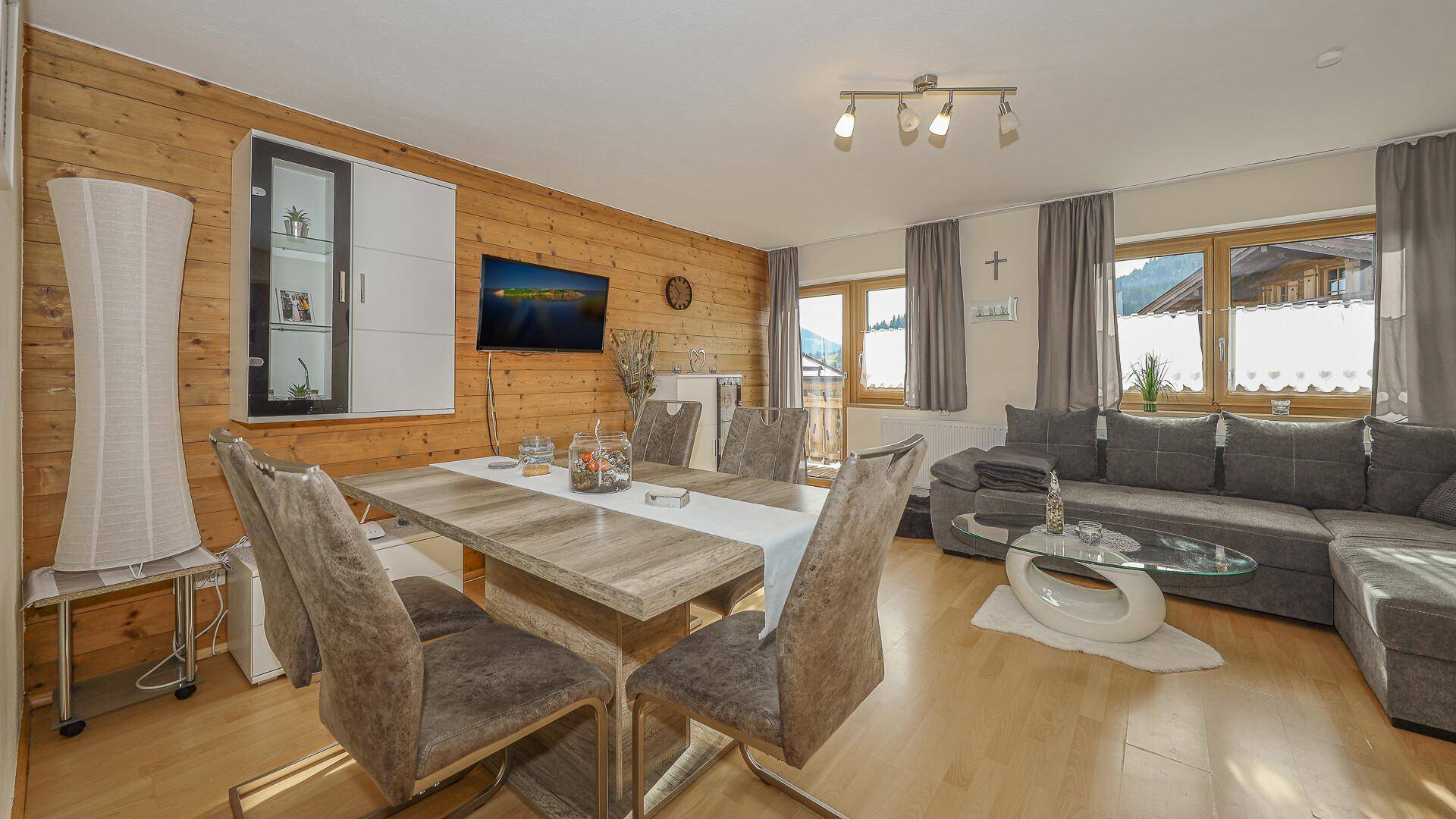 Moderner Wohn-Essbereich mit Holzwand, großem Sofa und Esstisch, hell und einladend.