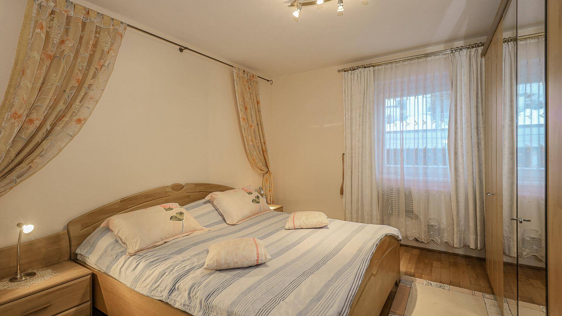 Gemütliches Schlafzimmer mit Doppelbett, Vorhängen und Holzmöbeln, hell und traditionell eingerichtet.