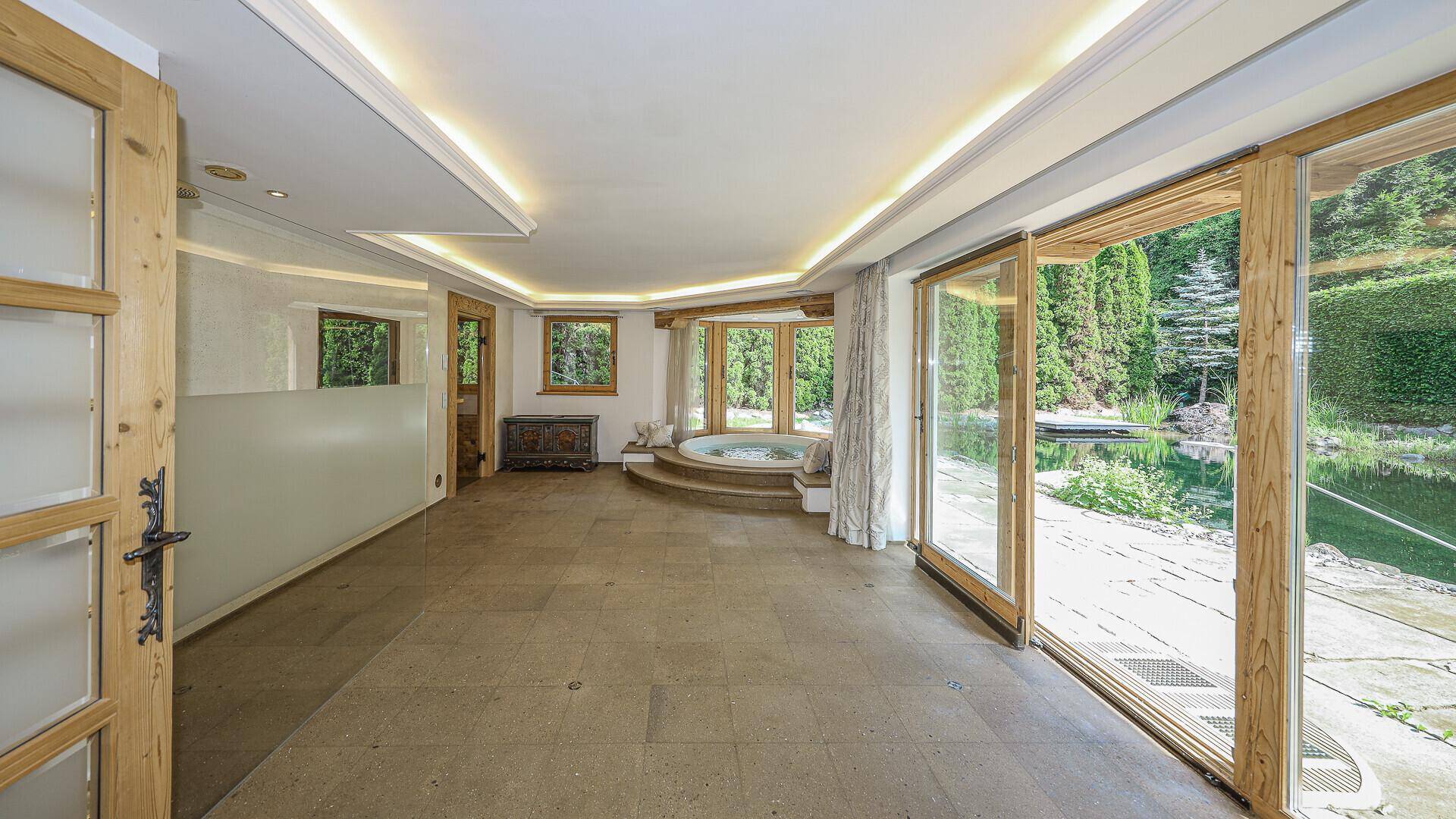Geräumiger Wellnessbereich mit Whirlpool, großen Fenstern und Zugang zum Garten.