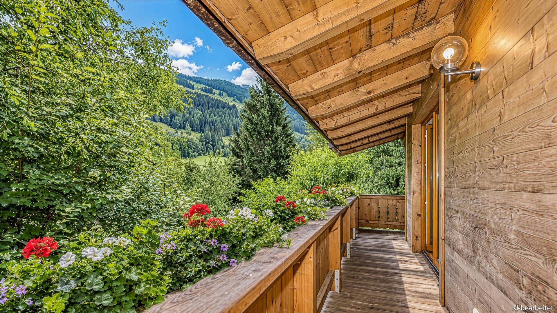 Langer Holzbalkon mit bunten Blumenkästen und weitem Blick auf die grüne Berglandschaft.