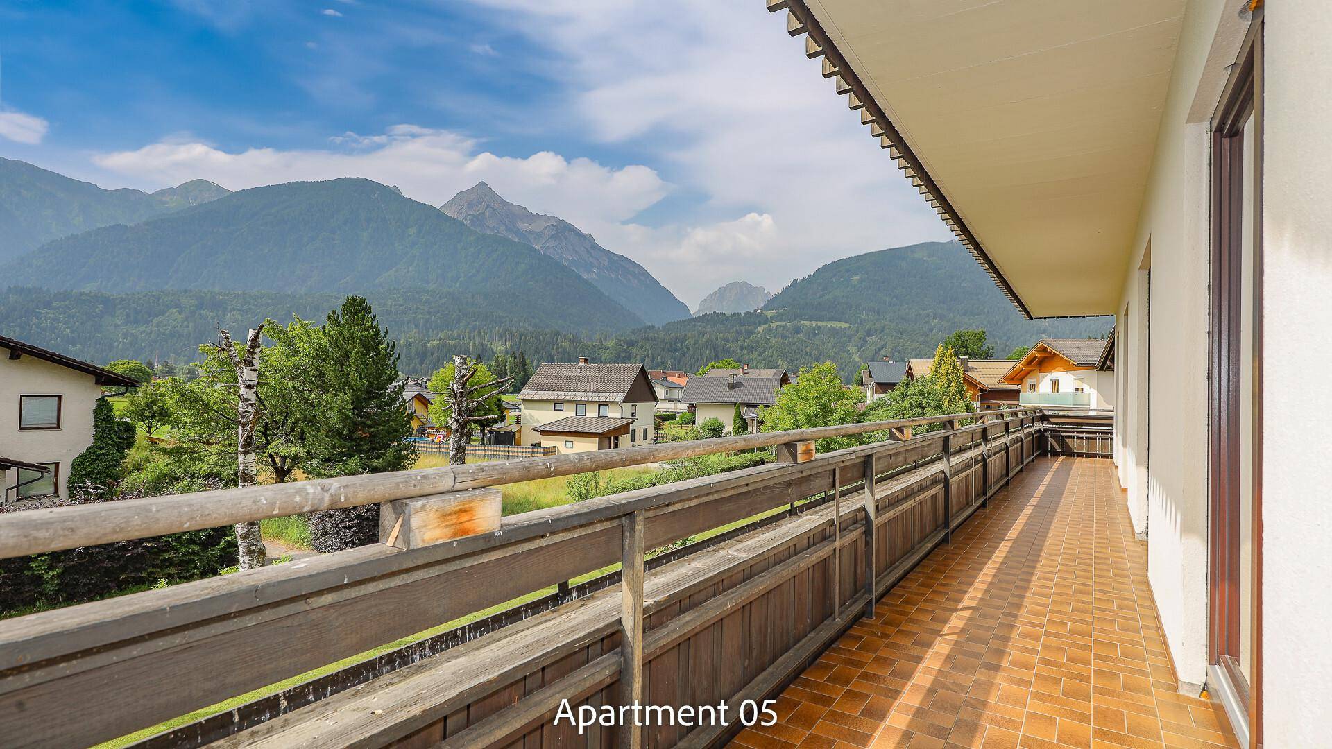 Balkon von Apartment 05 mit Fliesenboden und Holzgeländer, bietet einen weiten Blick auf die Berglandschaft.