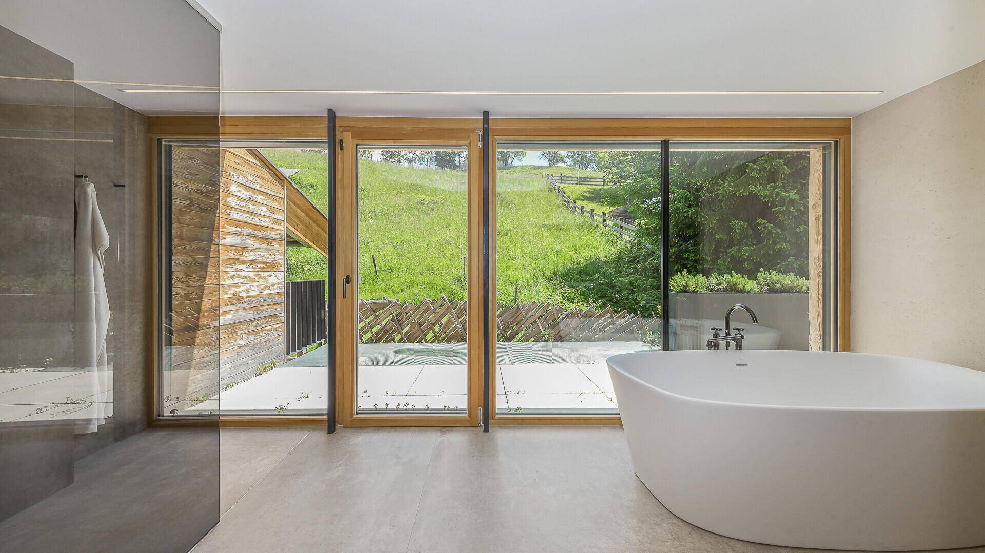 Modernes Badezimmer mit freistehender Badewanne, großer Fensterfront und Bergblick.