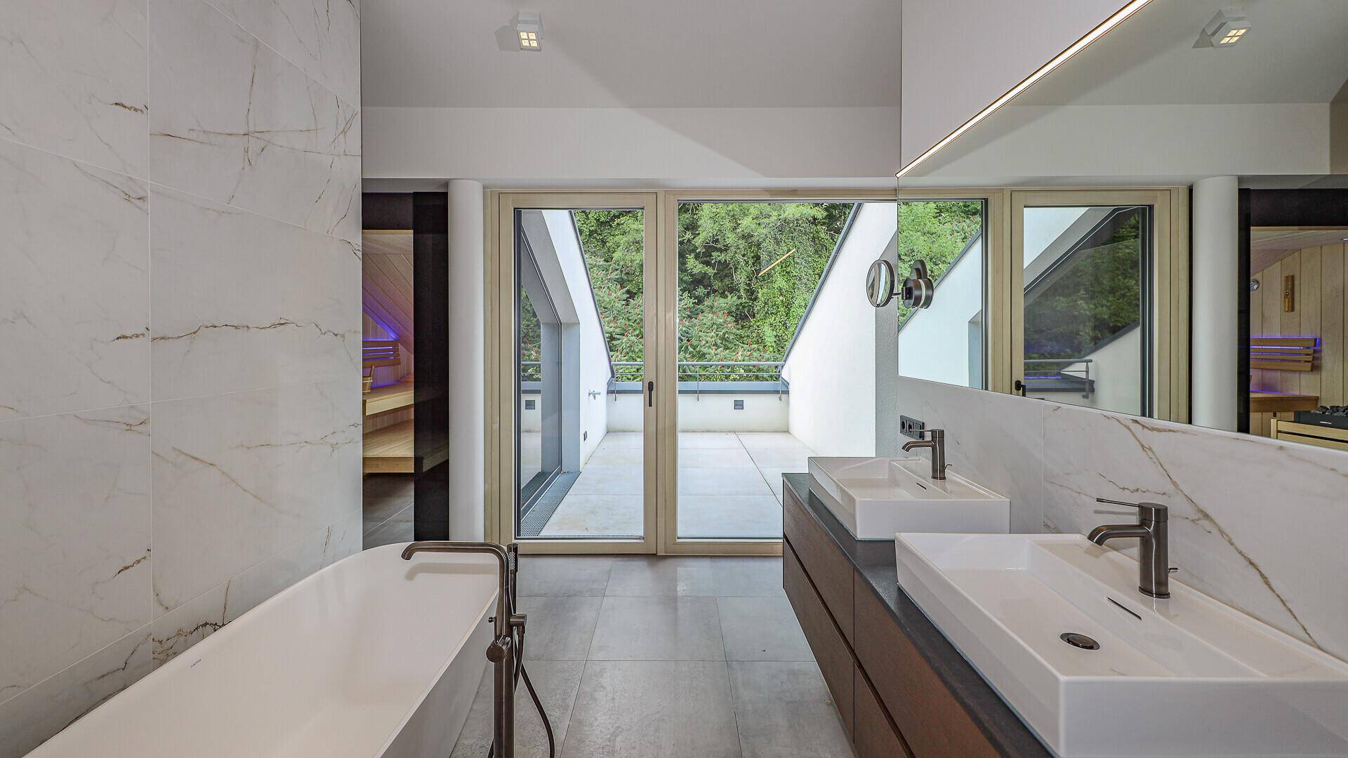 Elegantes Badezimmer mit Doppelwaschbecken, Marmorfliesen und großen Fenstern zur Terrasse.