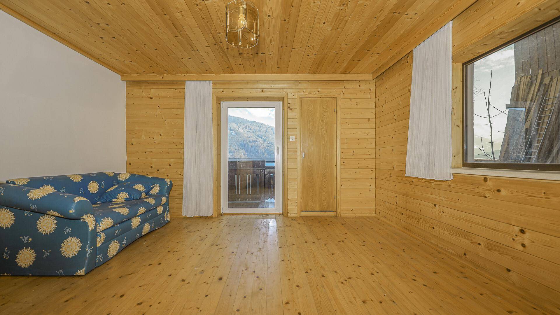 Wohnzimmer mit Holzvertäfelung, Holzdielenboden und Zugang zu einem Balkon mit Bergblick.