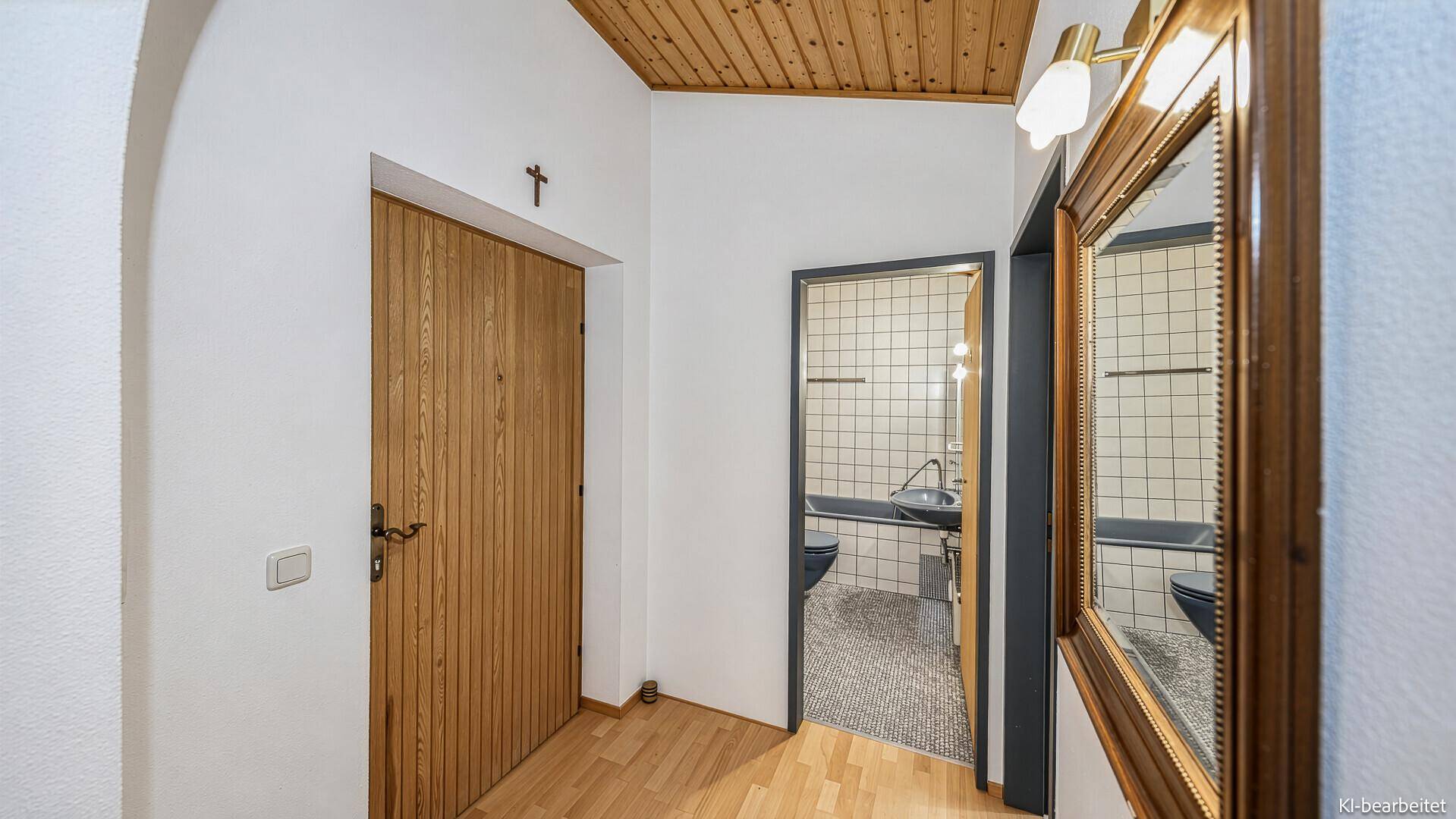 Heller Flur mit Holztür und Blick in ein Badezimmer mit dunkler Badewanne.