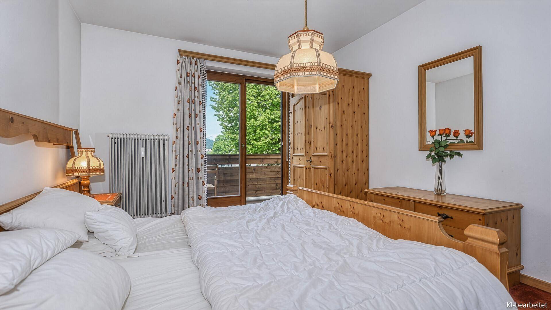 Helles Schlafzimmer mit Holzbett, Balkonzugang und Blick auf die grüne Umgebung.