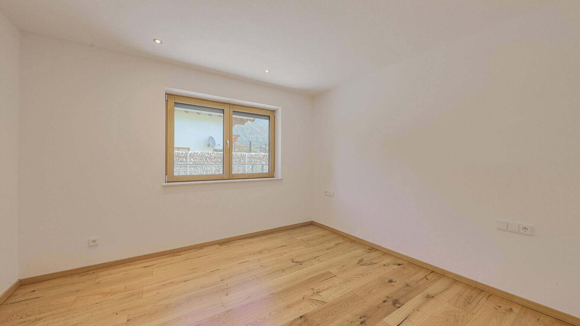 Leeres Schlafzimmer mit Holzboden, weiß gestrichenen Wänden und Fenster.