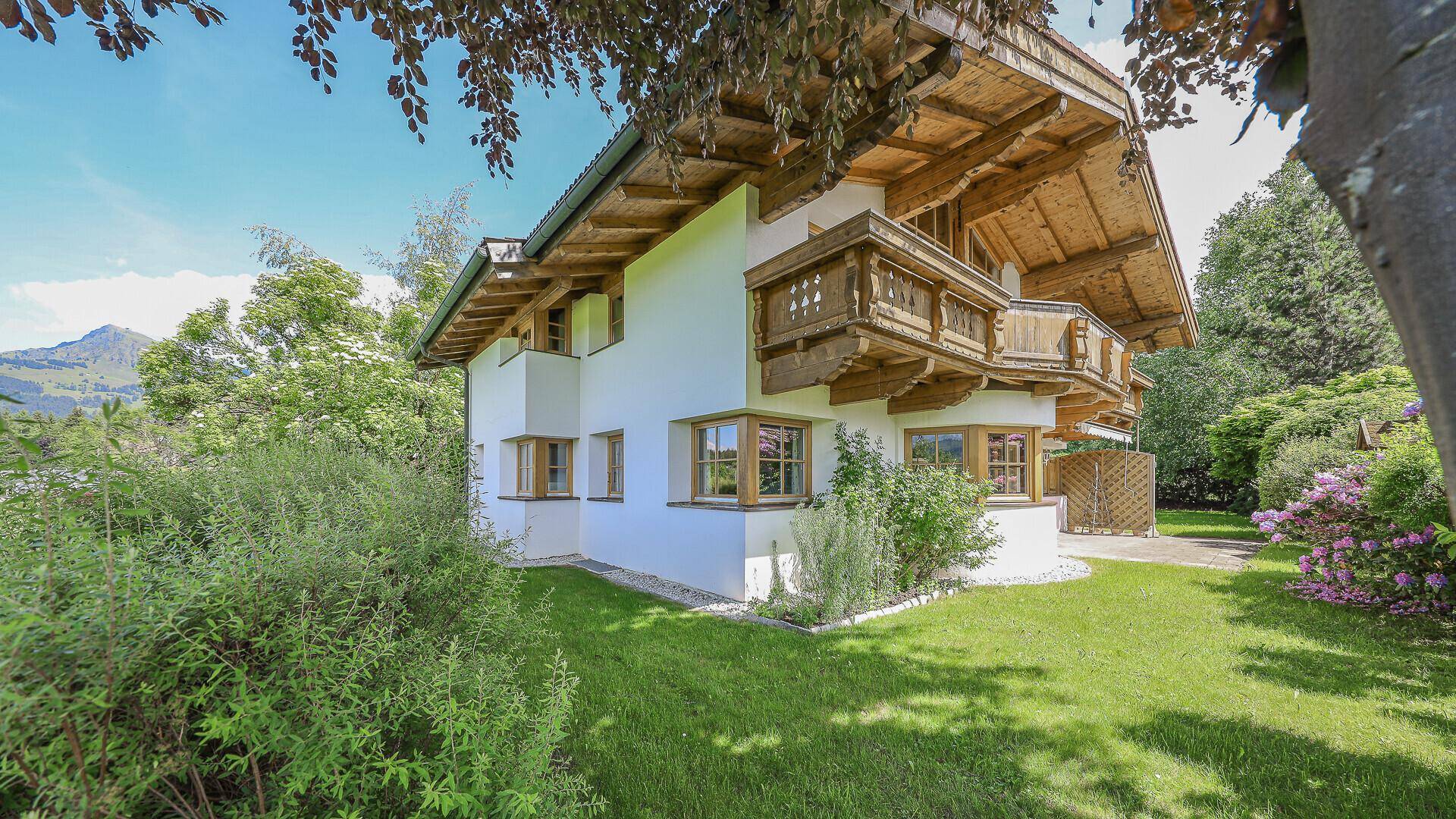 Gepflegter Garten mit grüner Rasenfläche und blühenden Sträuchern um das traditionelle Chalet.