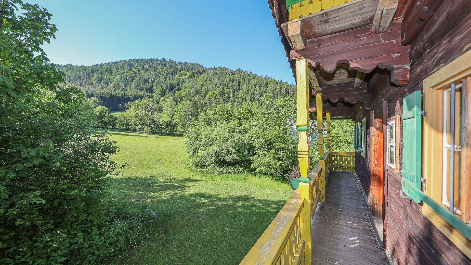 Traditioneller Holzbalkon mit Blick auf die umliegende grüne Landschaft und bewaldete Hügel.