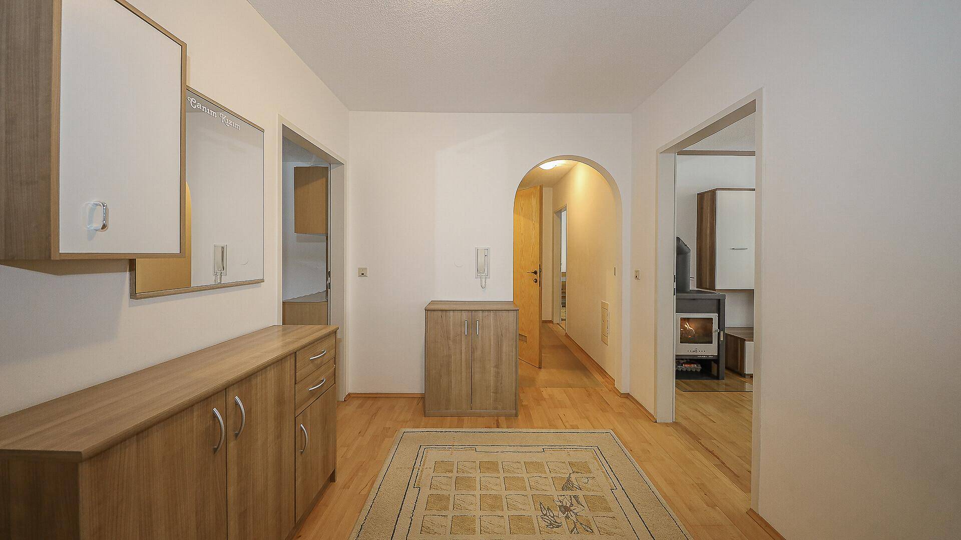 Heller Flur mit Holzmöbeln, Teppich und Zugang zu weiteren Räumen.