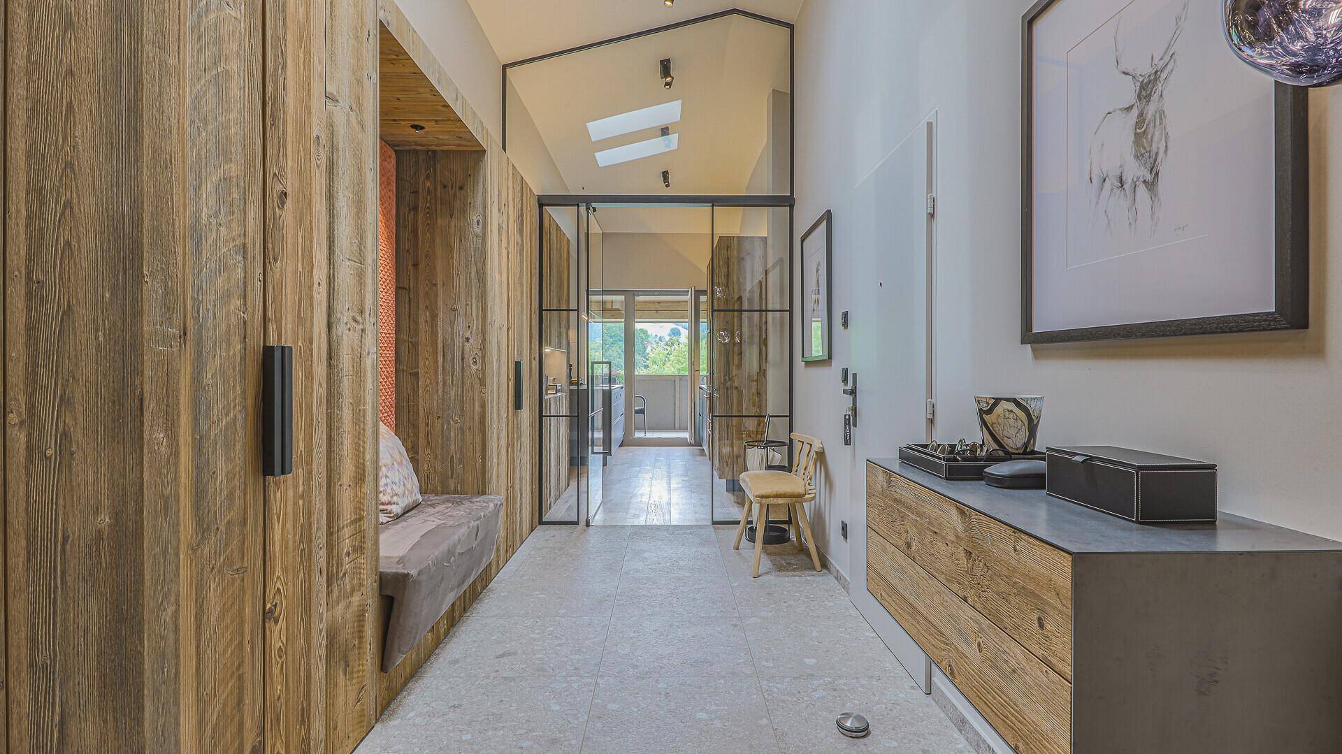 Moderner Eingangsbereich mit Holzelementen, Kunstwerken und Blick durch eine Glastür.