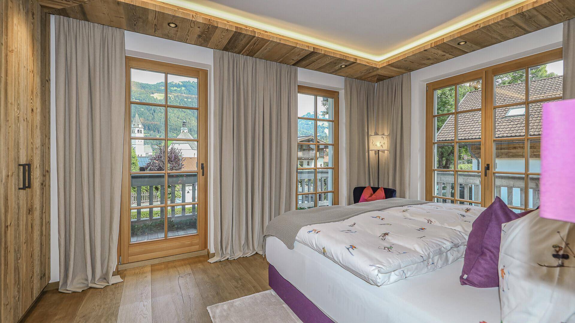 Helles Schlafzimmer mit Balkonzugang, Holzboden und Blick auf die umliegende Landschaft.