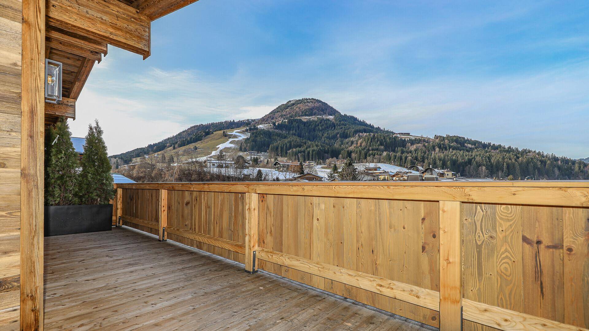 Sonniger Balkon mit Holzboden und weitem Panoramablick auf die verschneiten Berge.