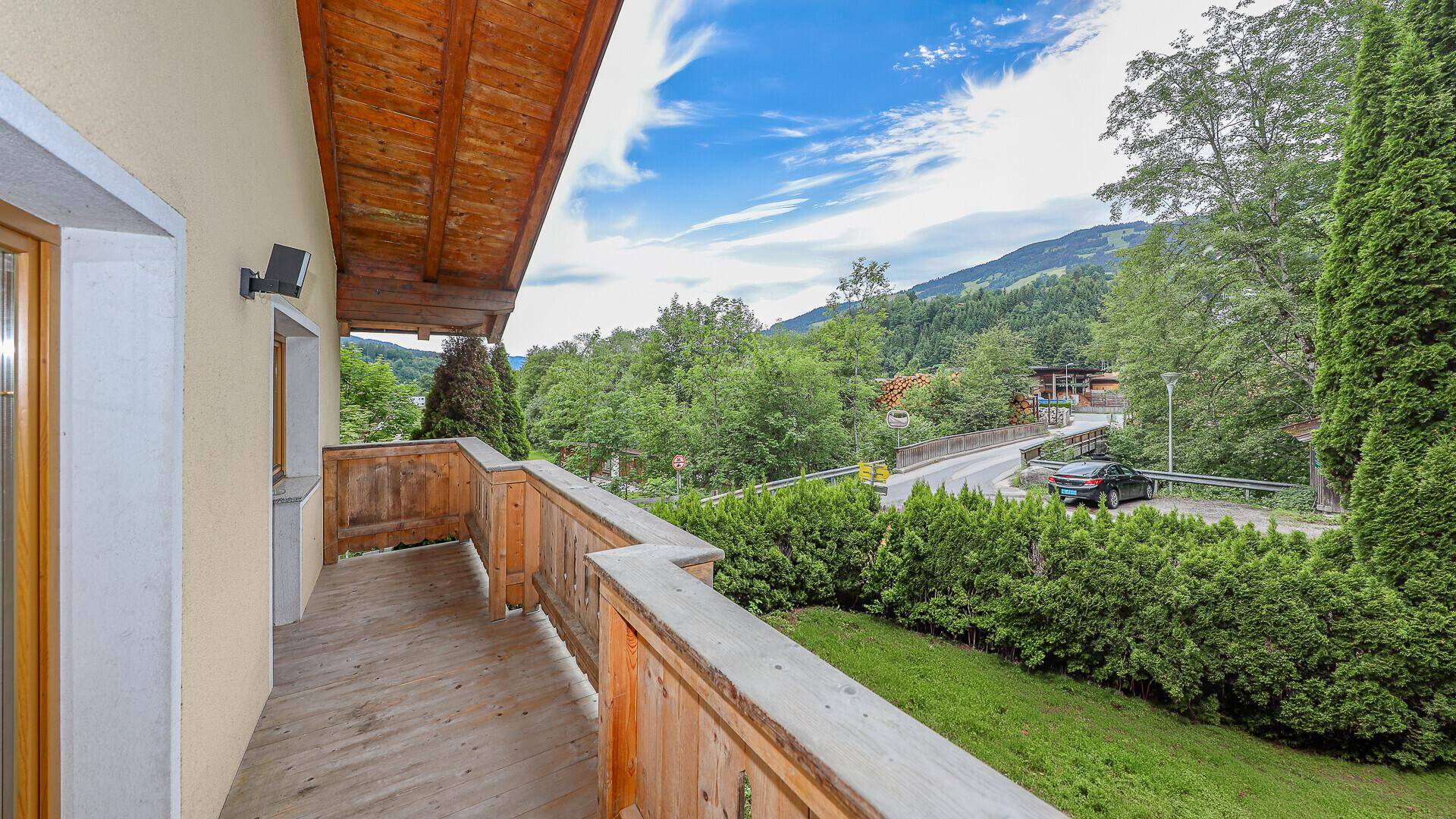 Holzbalkon mit weitem Blick über die Straße, umliegende Häuser und grüne Hügel.