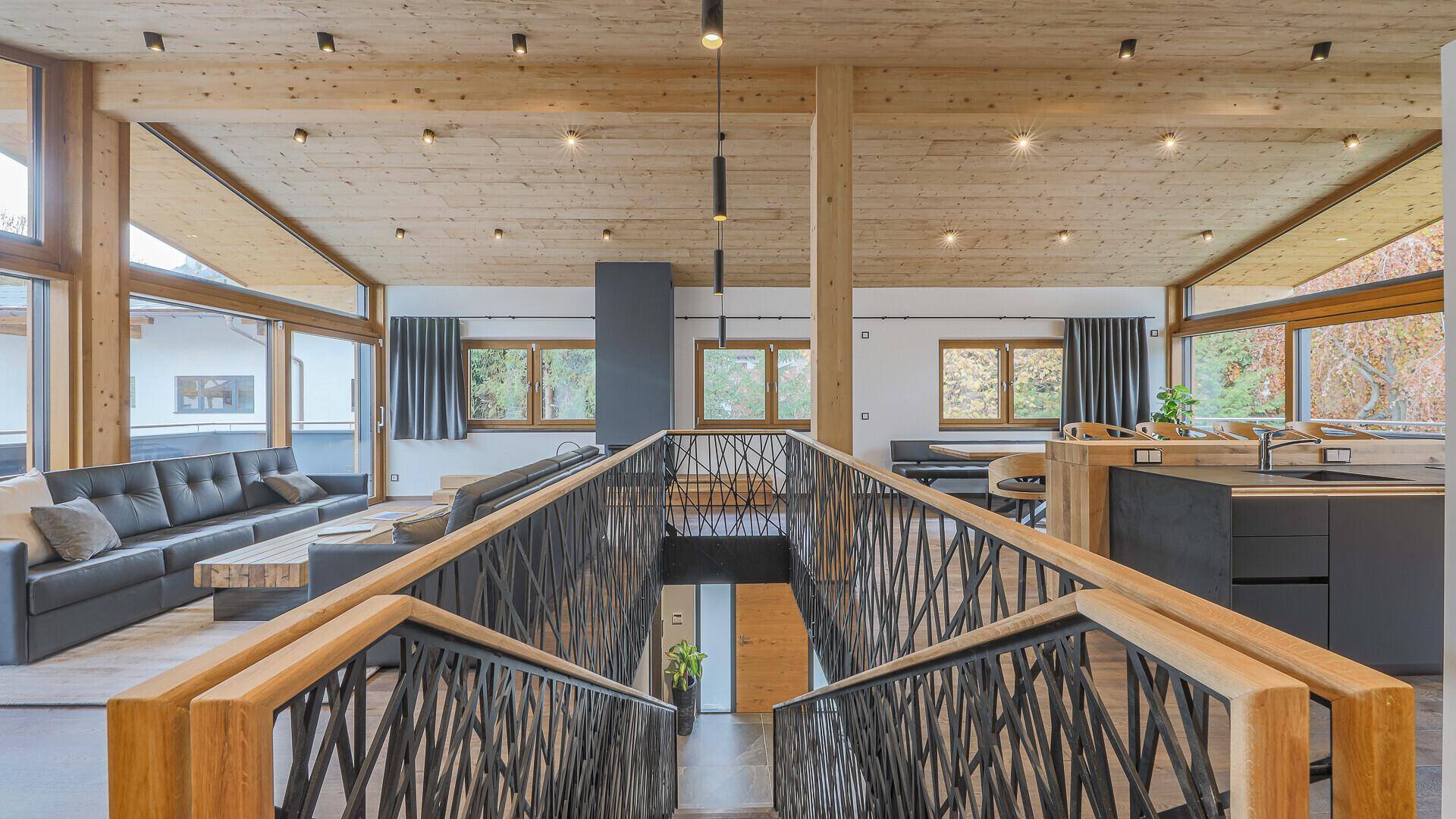 Offener Wohnbereich mit Holzdecken, moderner Treppe und Blick auf die umliegende Natur.