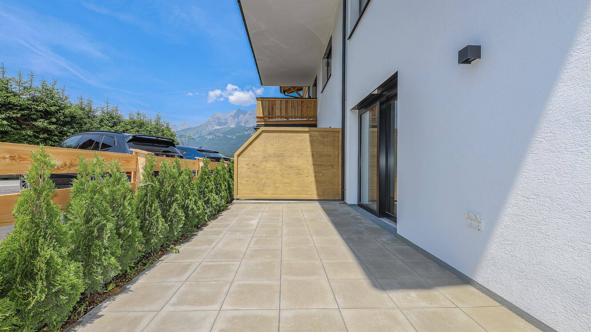 Gepflasterter Terrassenbereich mit Hecke und Bergblick.